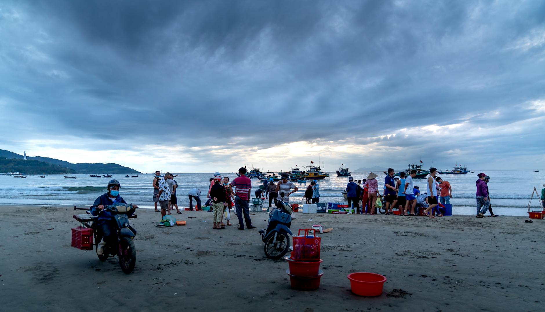 Fishermen gather on a beach under a cloudy sky, preparing their catch.