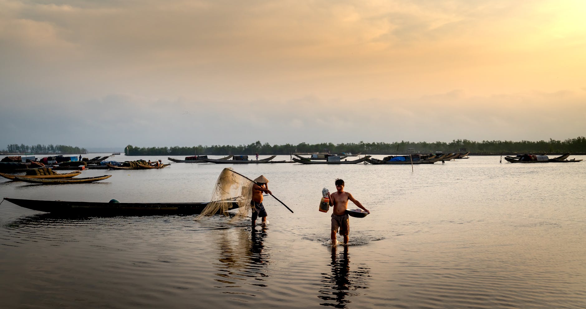 Two men fishing in traditional boats during a tranquil sunrise on a river.