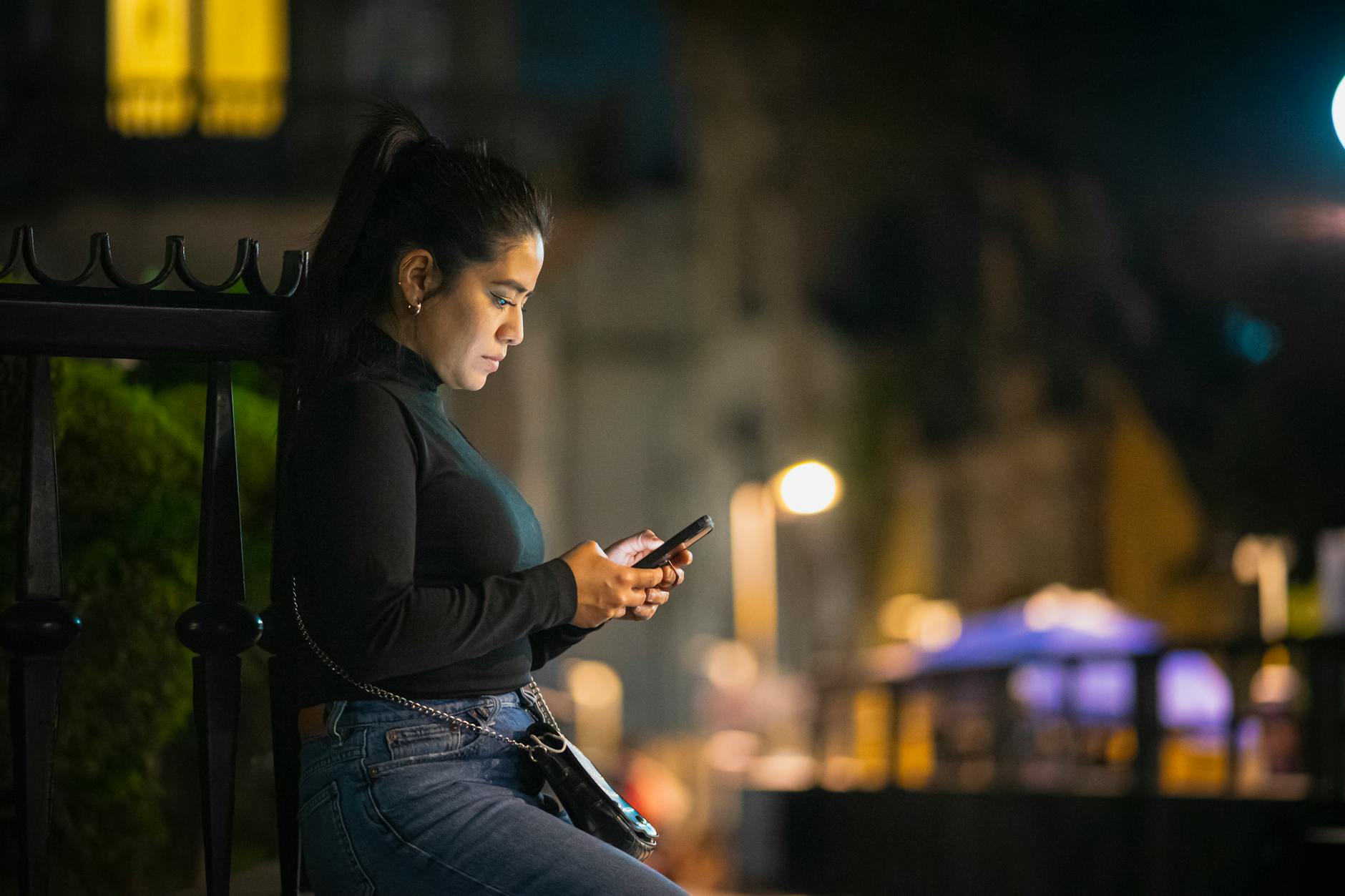 A woman is engrossed in her smartphone on a bustling street in Mexico City at night.