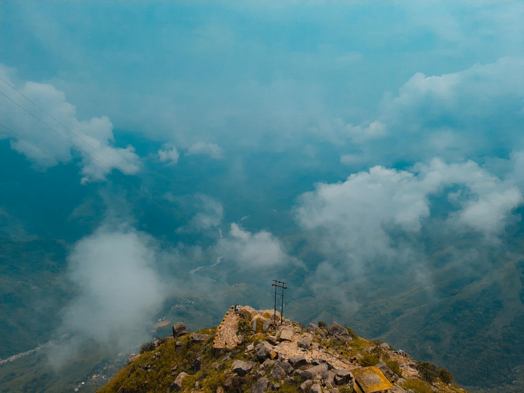 High-angle view of a rocky mountain summit surrounded by clouds in a lush green valley.