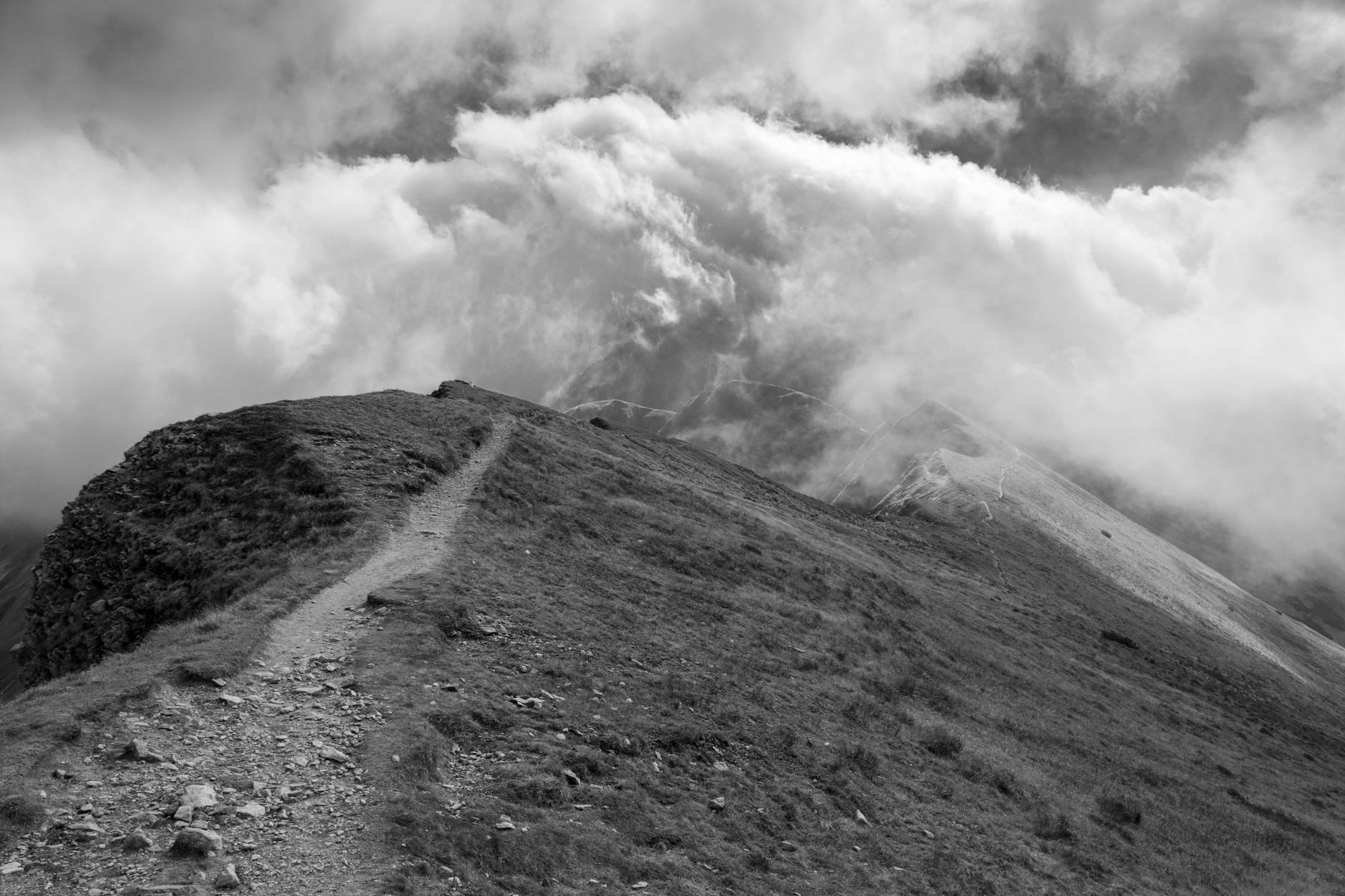 A captivating black and white image of a mountain path leading into swirling clouds, creating a dramatic landscape scene.