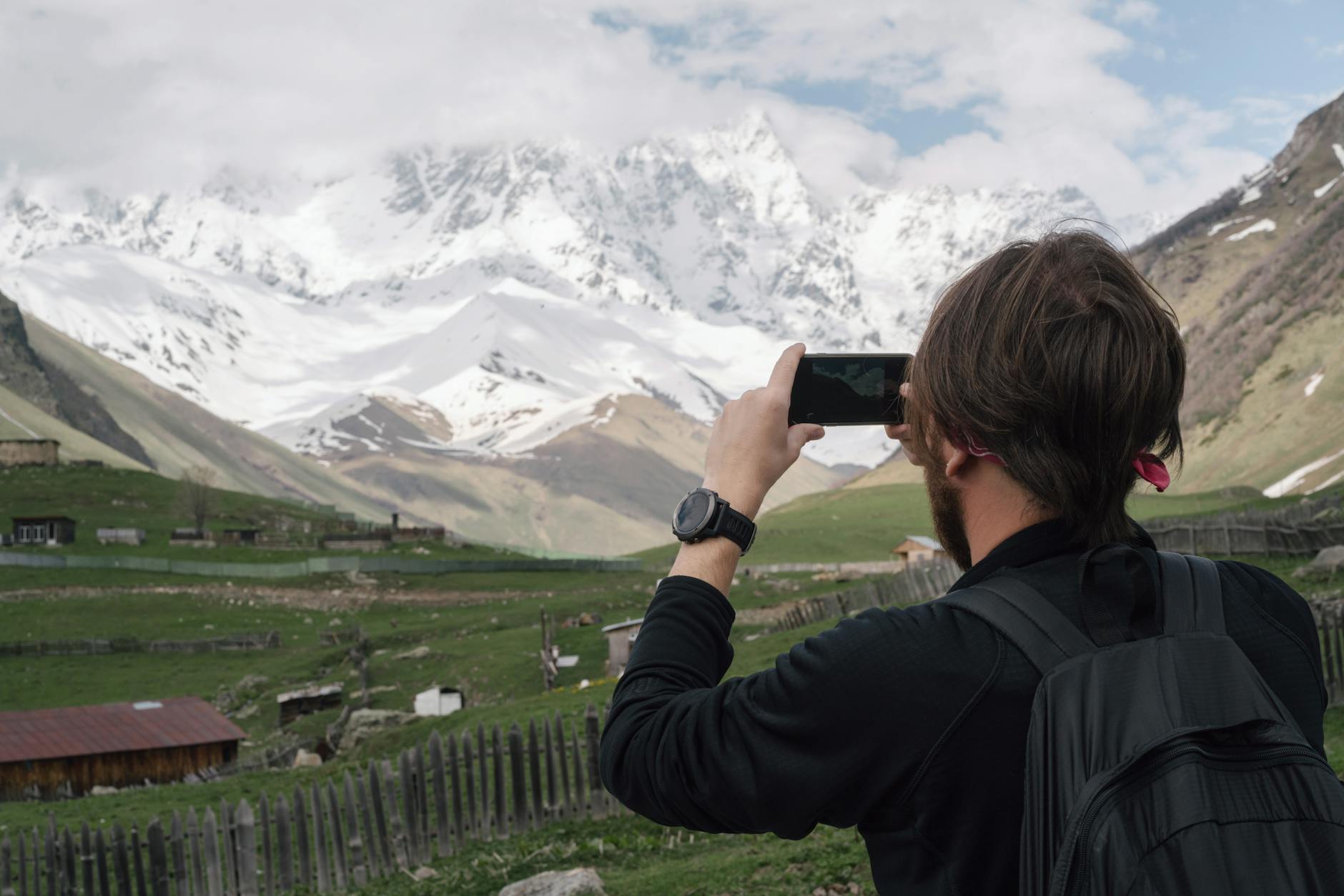 A man captures the snowy mountain scenery in a rural village setting with his smartphone.