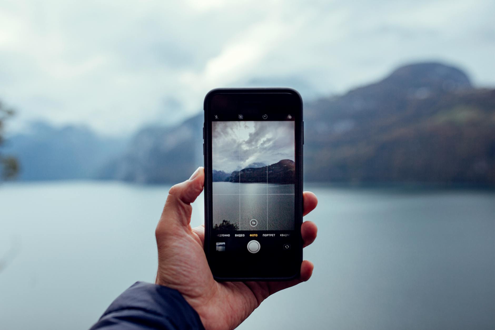 A person photographs a scenic lake view in Switzerland using a smartphone.