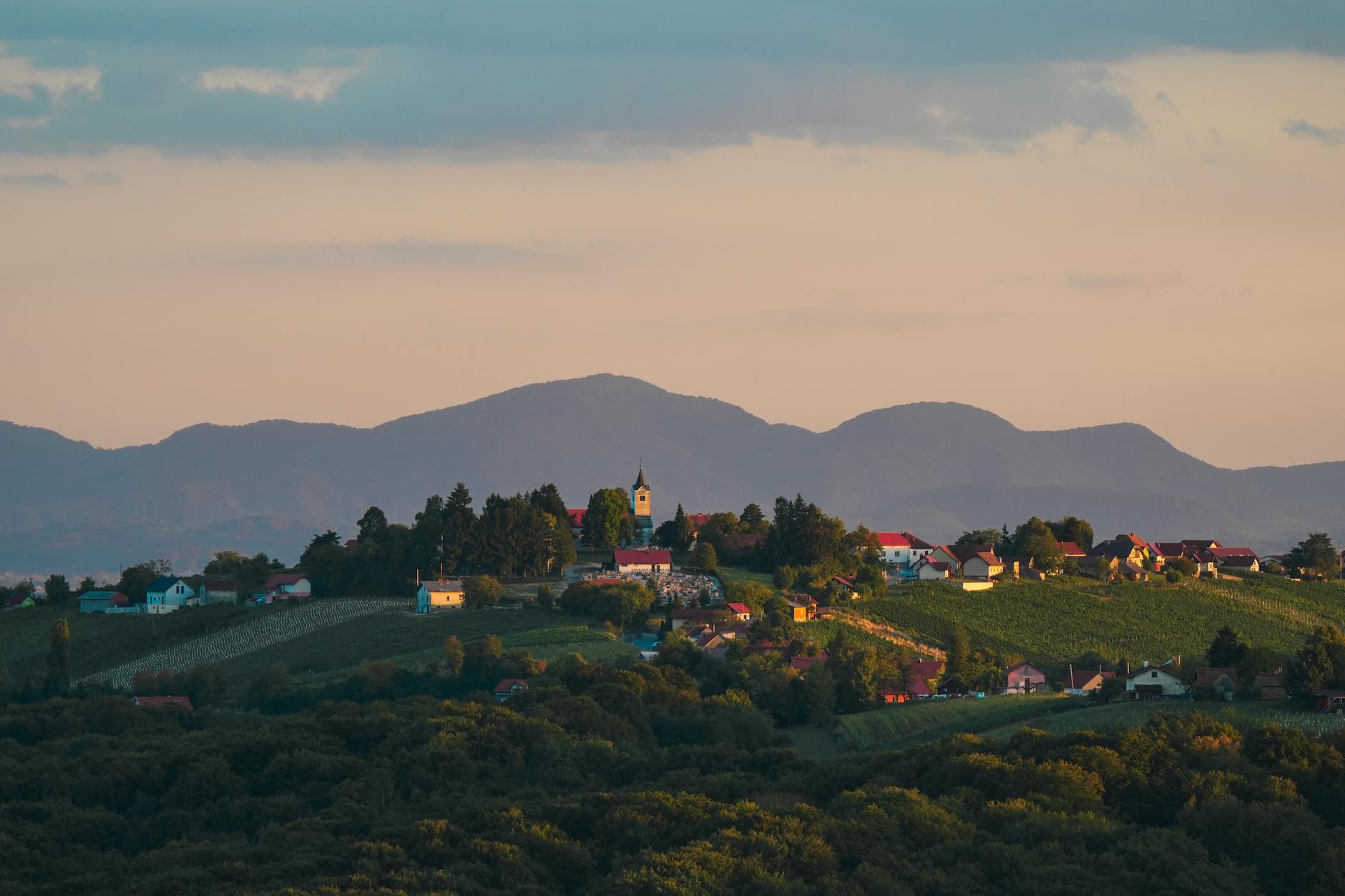 Beautiful village landscape at sunset with a church, vineyards, and mountains in the background.