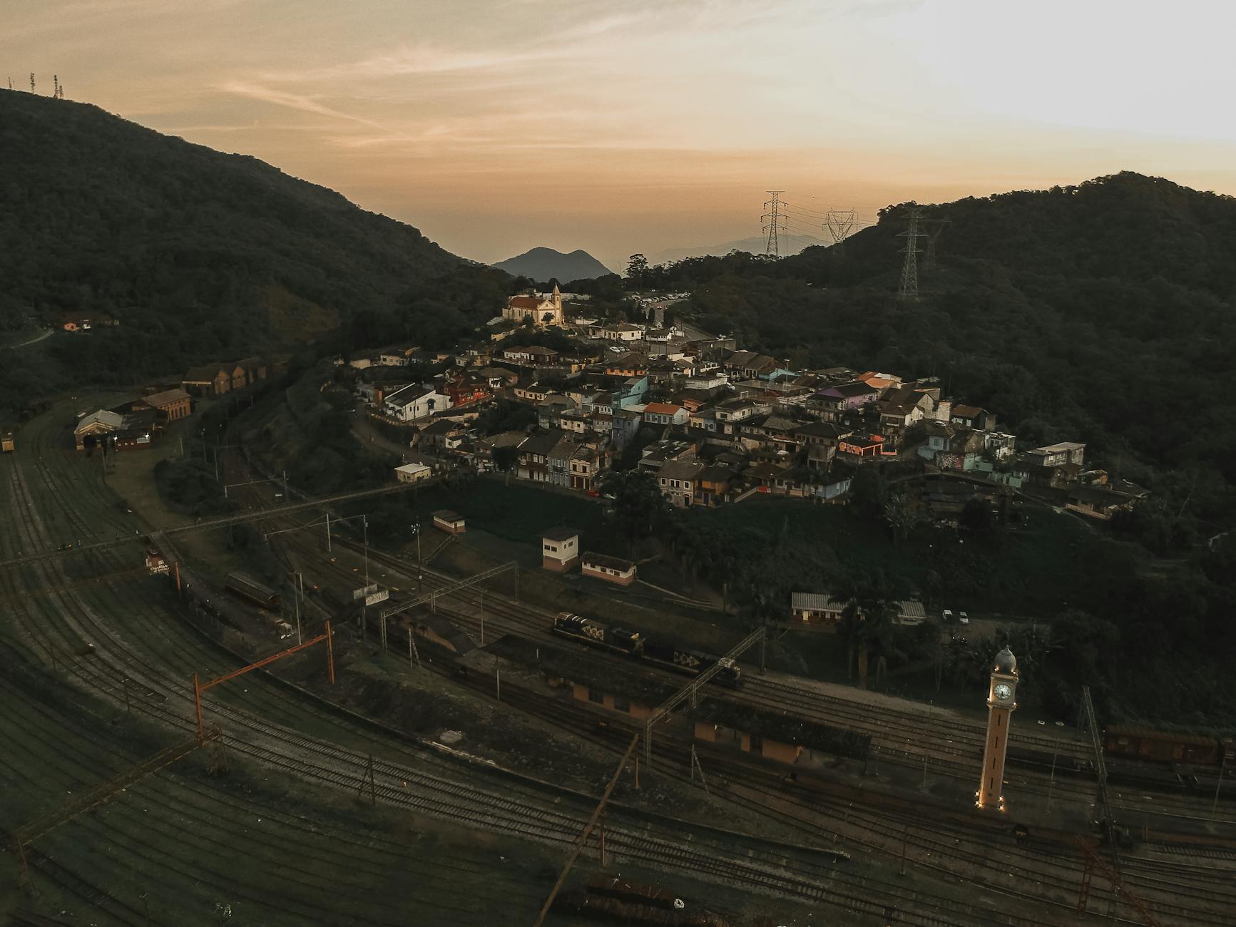 A scenic aerial shot capturing a small town, railway, and green hills at sunset.