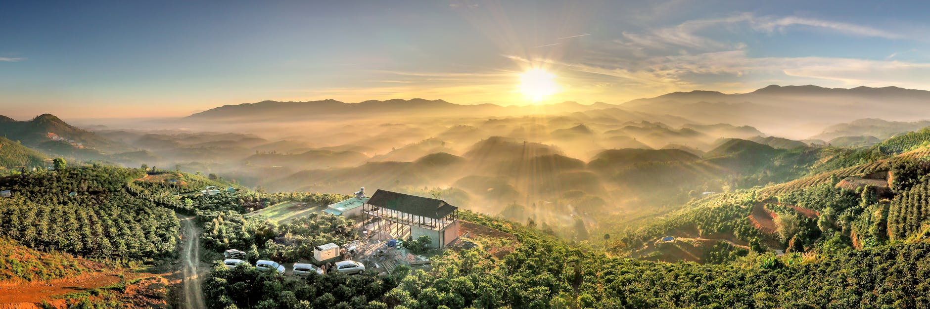 Panoramic view of a village surrounded by lush hills at sunrise, enveloped in mist.