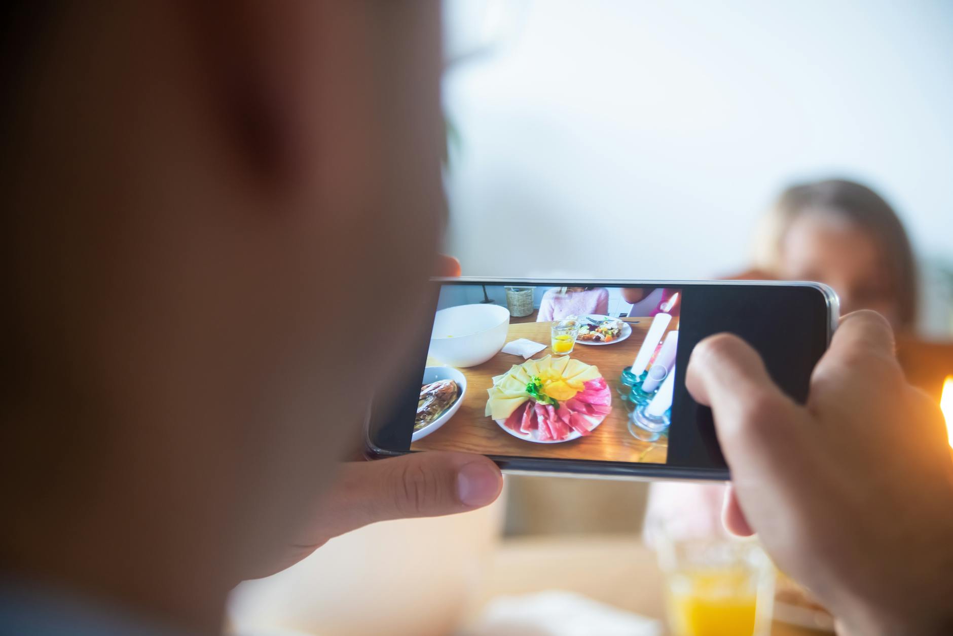 Close-up of a person taking a photo of a colorful food platter with a smartphone indoors.