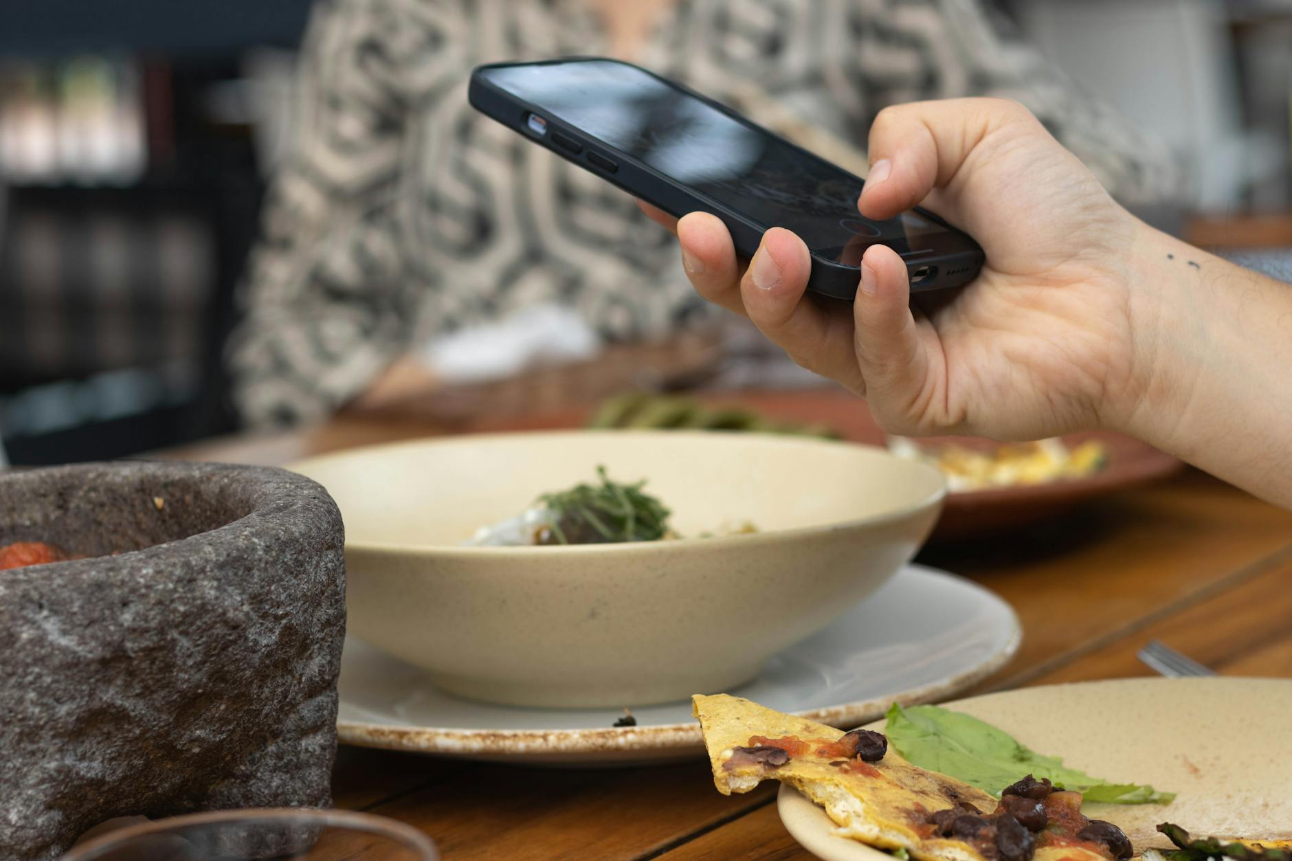 A person takes a photo of their meal using a smartphone at a restaurant table.