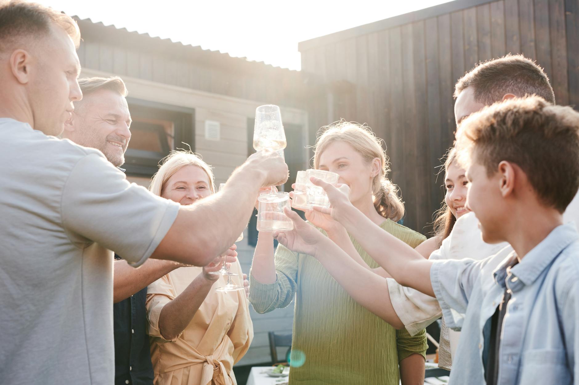 A group of friends and family cheerfully toasting with drinks outside during the day.