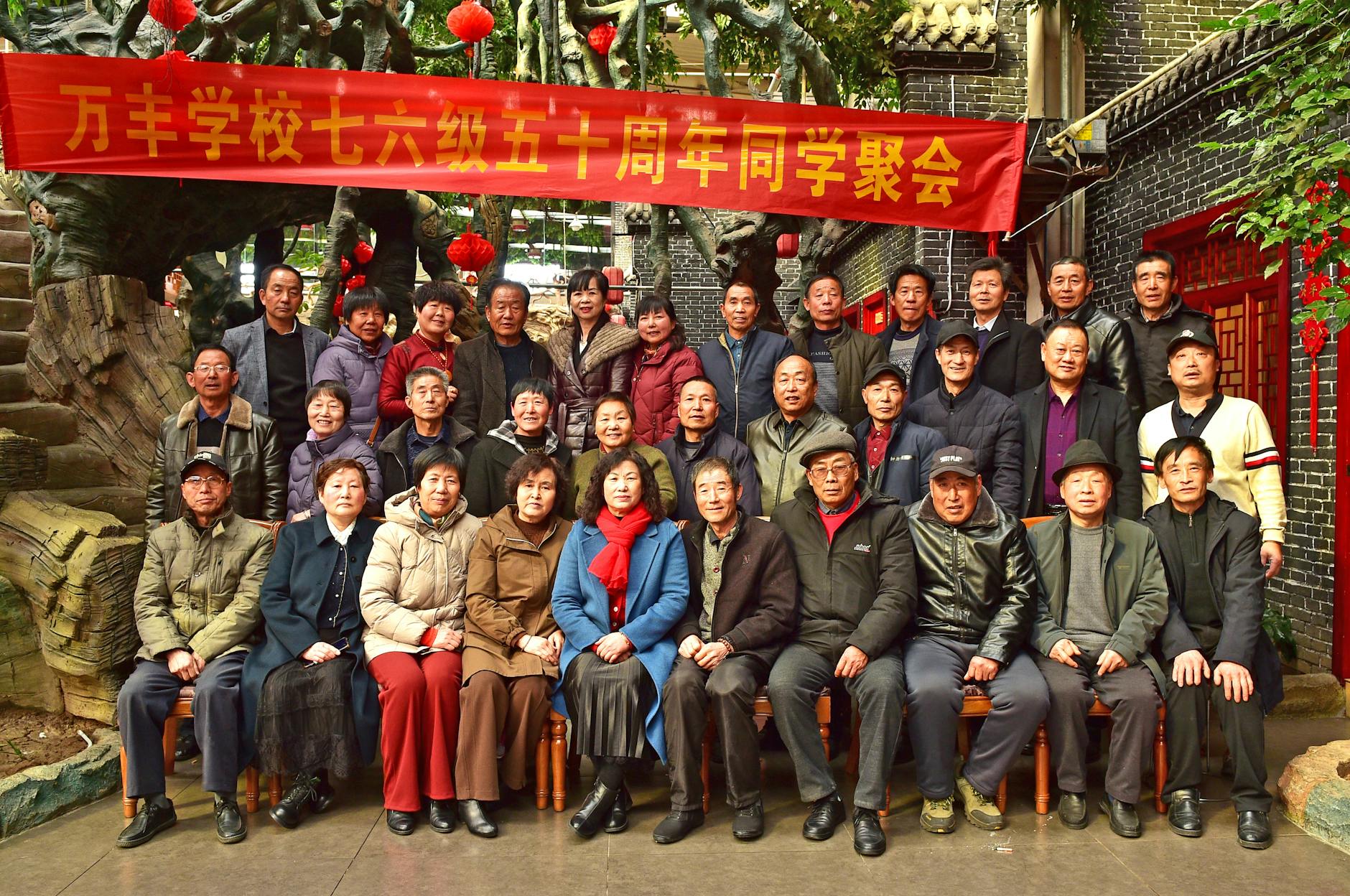 A group of alumni gather outdoors for a reunion event under a banner.