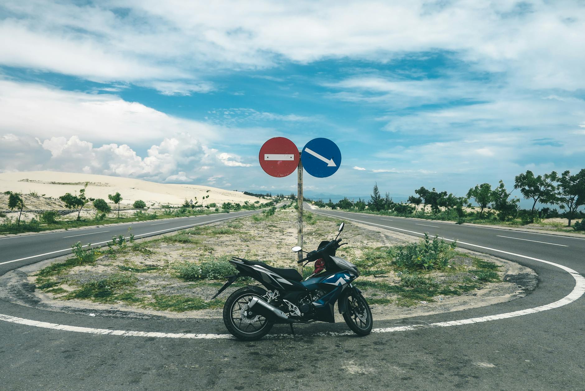A motorbike parked at an empty road intersection in Phan Thiết, Vietnam, under a clear blue sky.