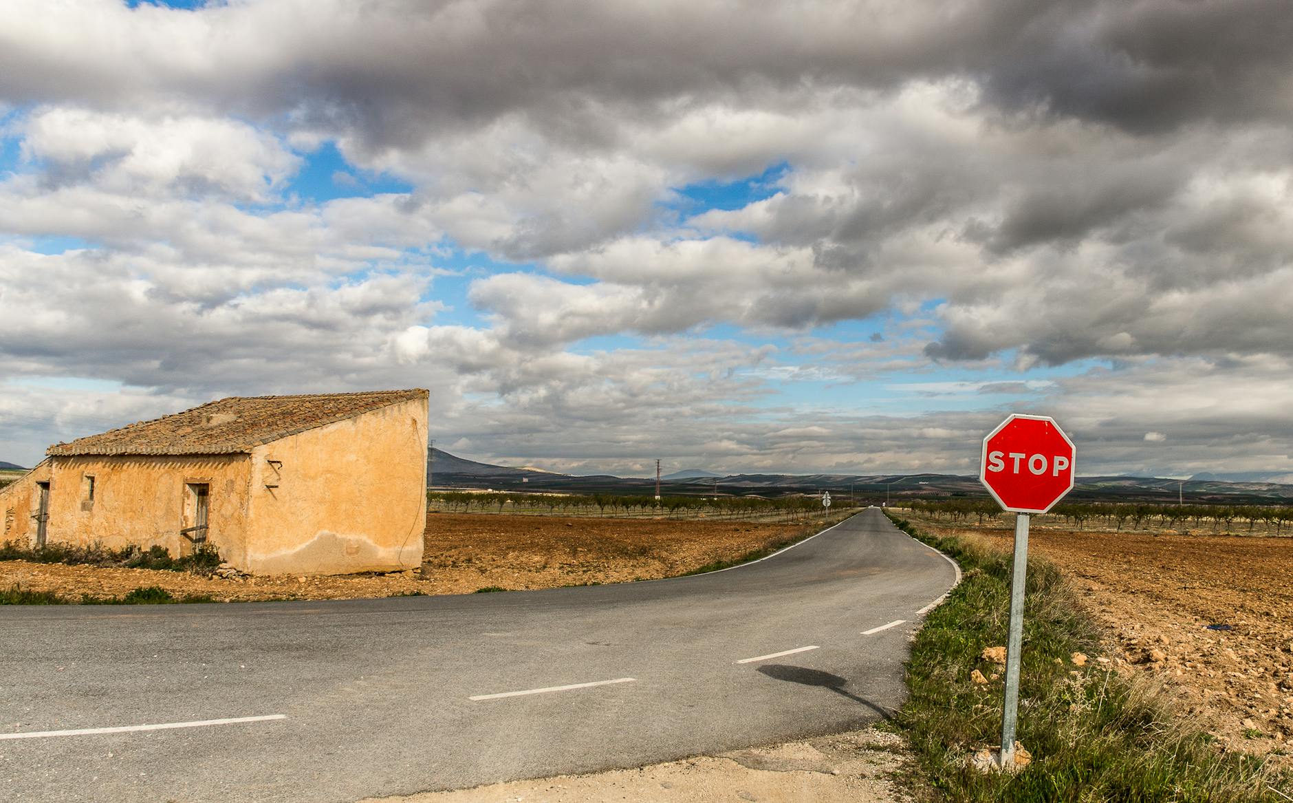 A rural landscape featuring a road, a stop sign, and a small building under cloudy skies.