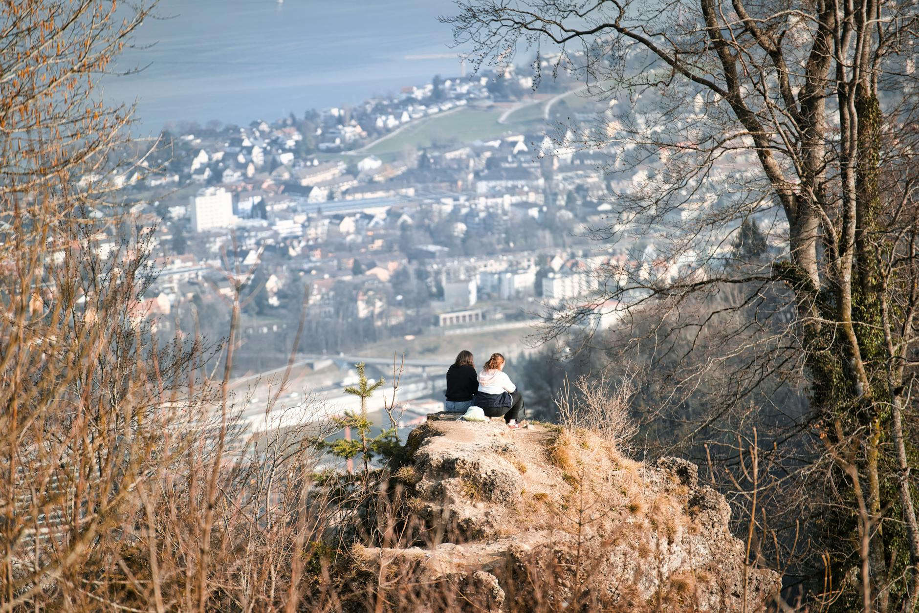 Two people on a hilltop overlook a scenic cityscape in early spring.