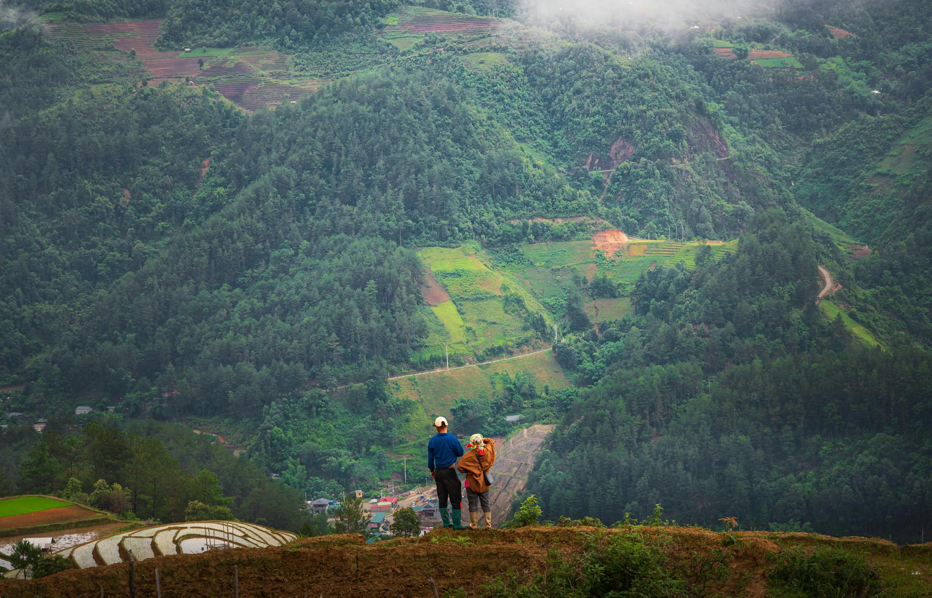 A couple enjoys a serene view of a lush mountain valley with terraced fields.