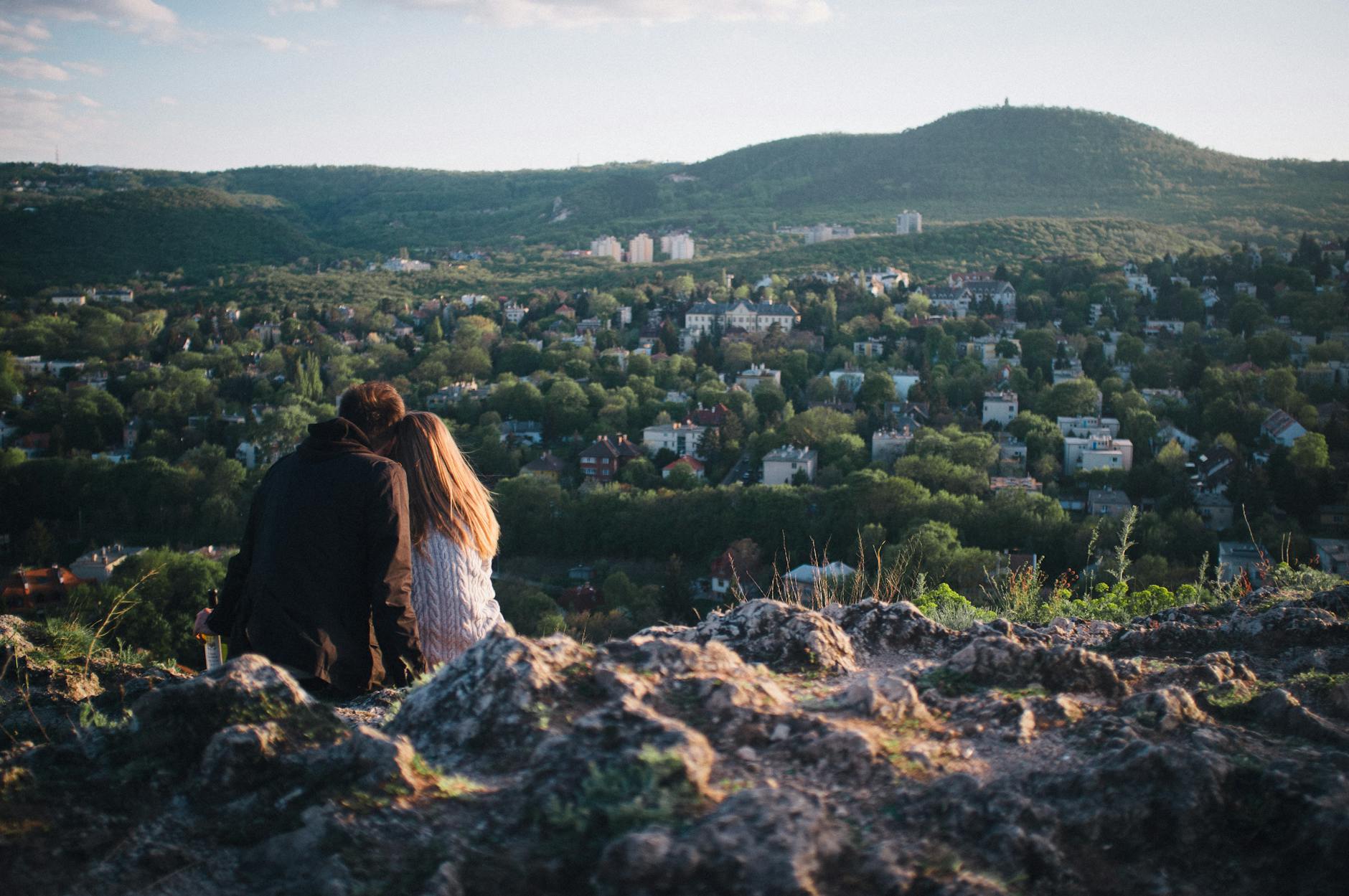 A couple enjoying a scenic view of Budapest from a rocky hilltop during the day.