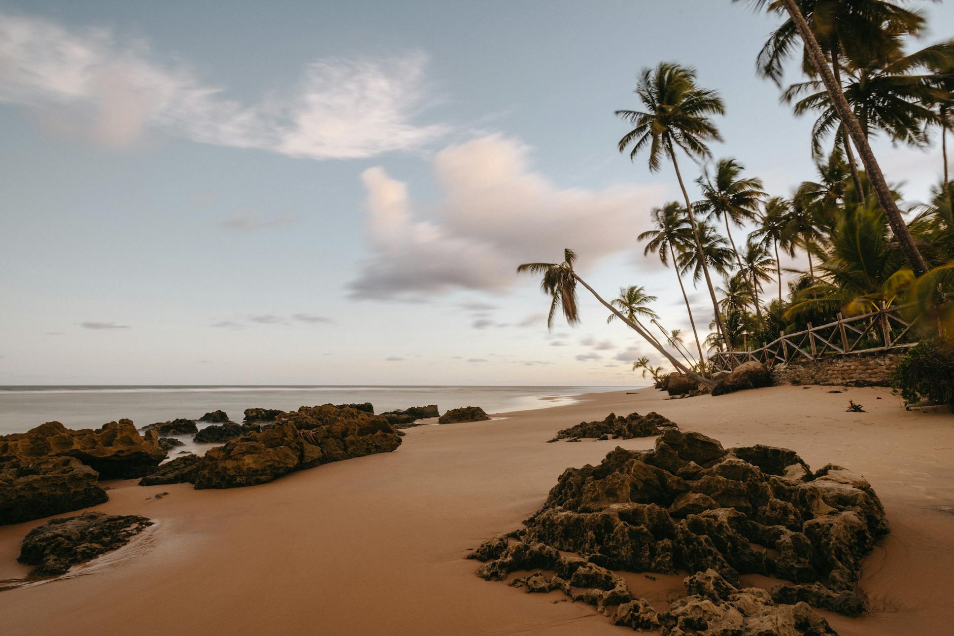 Serene tropical beach with palm trees and rocky formations at sunset, perfect for a tranquil getaway.