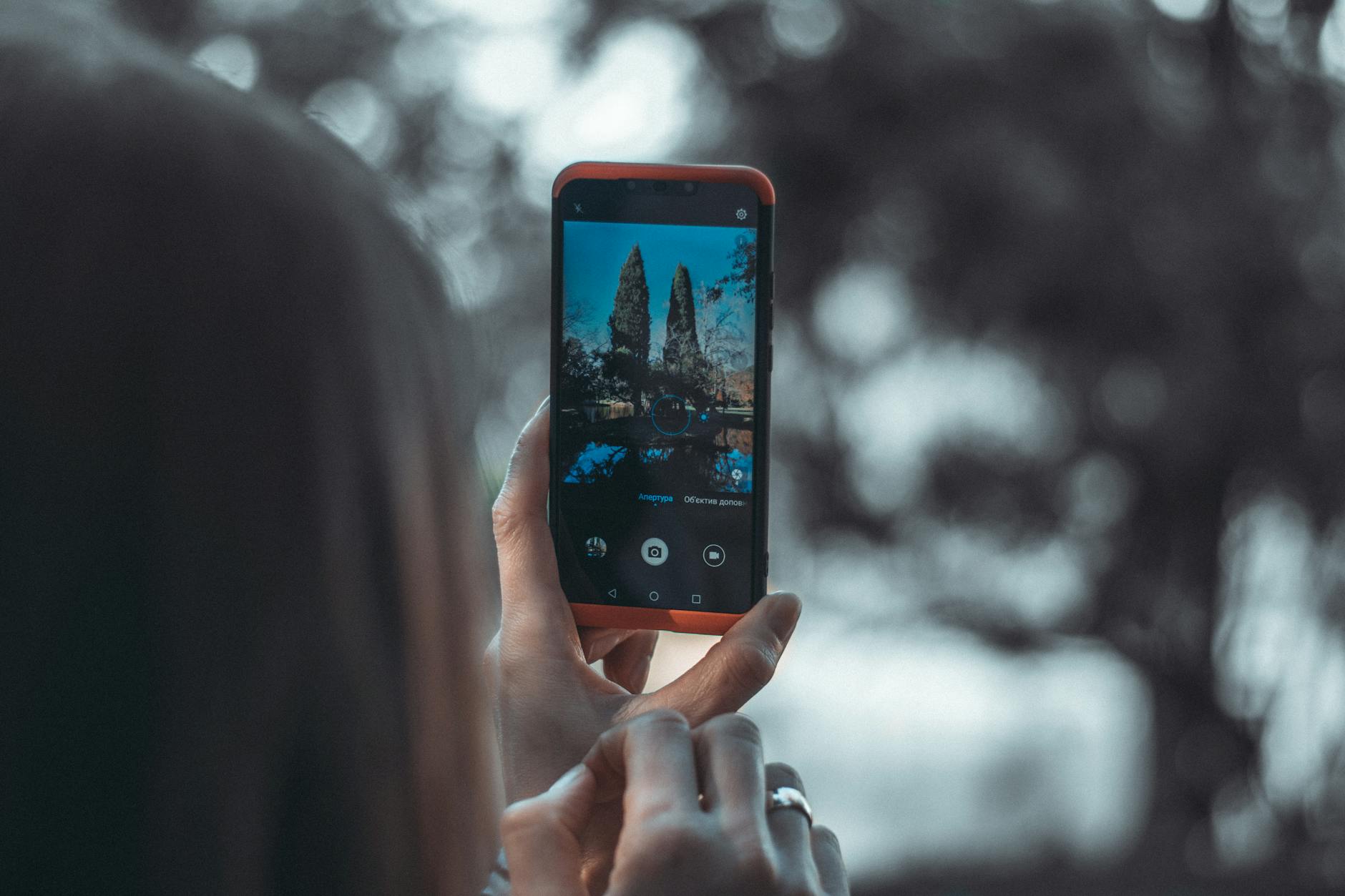 A person takes a photo in nature using a smartphone, capturing trees in focus.
