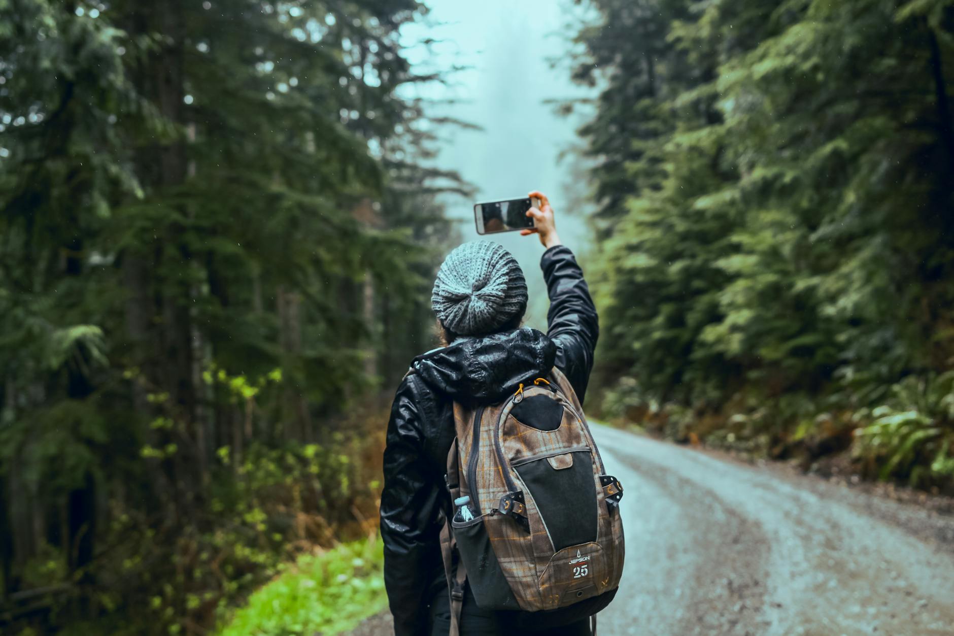 Woman takes scenic selfie on forest trail, capturing nature's beauty.
