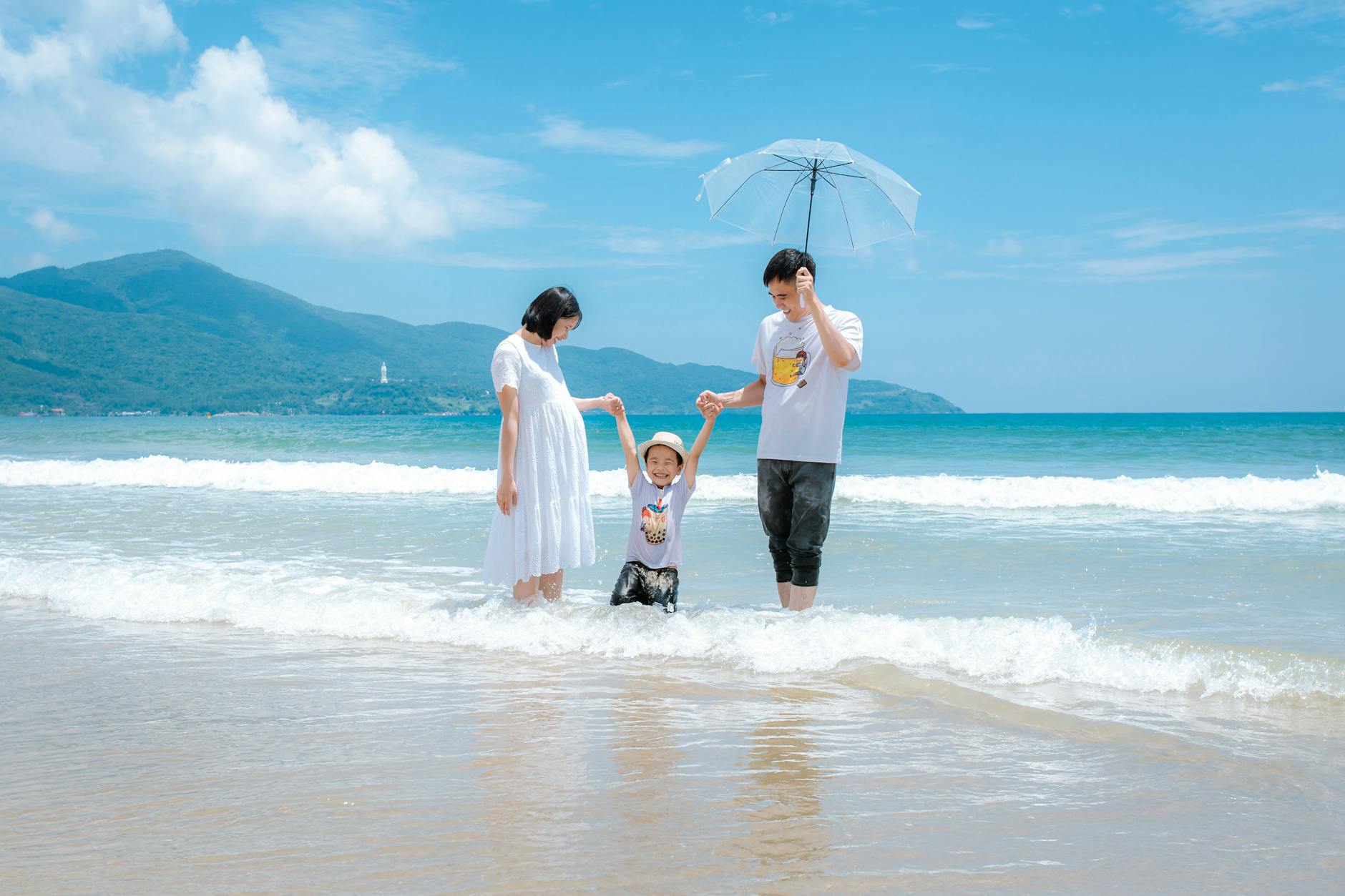 Happy family enjoying a sunny day at Da Nang Beach, Vietnam, playing in the waves.