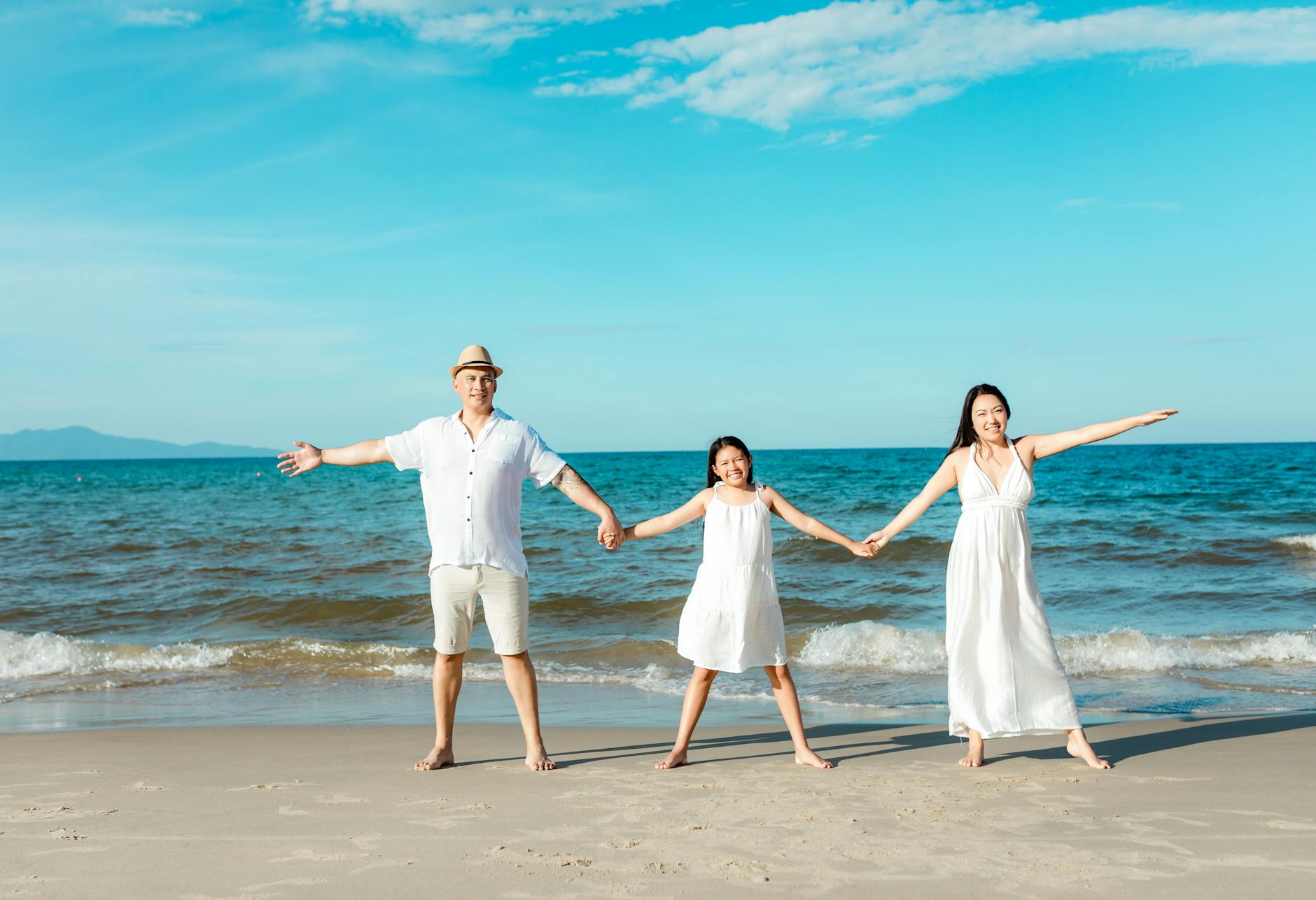 Happy family holding hands on a sunny beach in Hoi An, Vietnam.