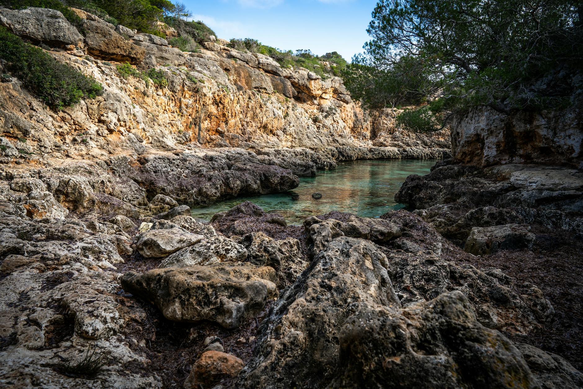 Exploring an eroded rocky cove with crystal-clear water and lush greenery.