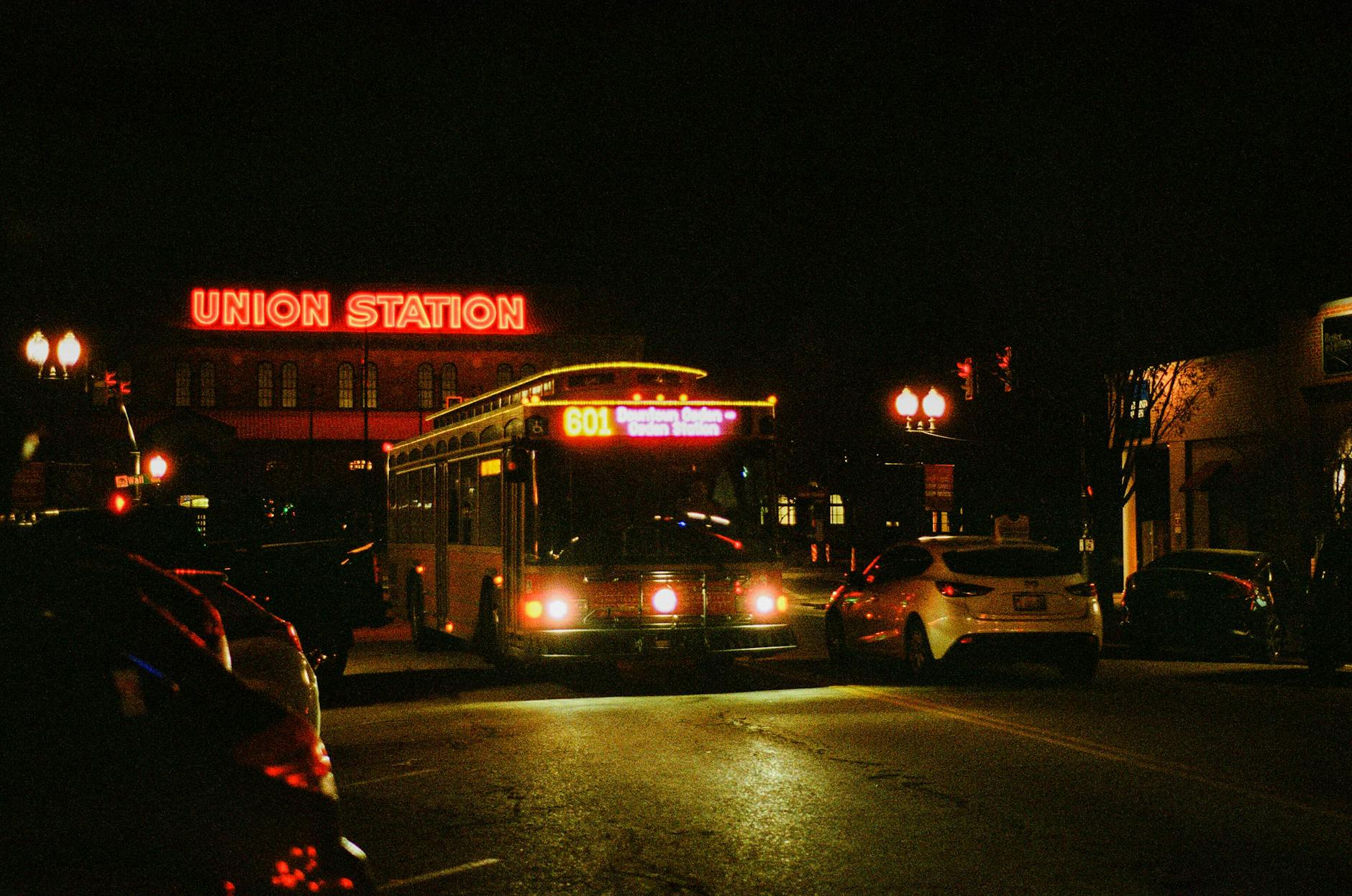 Nighttime scene of Union Station with a bus and neon lights highlighting the urban street.