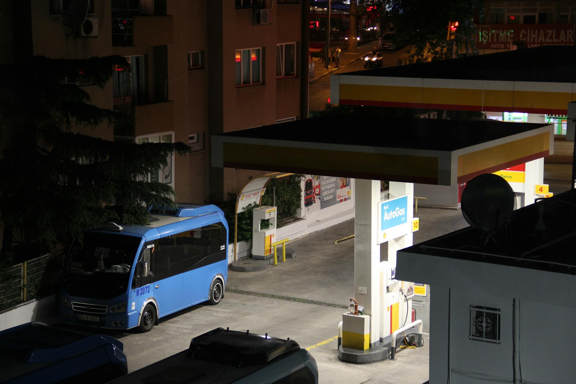 A nighttime urban scene featuring a gas station and a parked bus in a city environment.