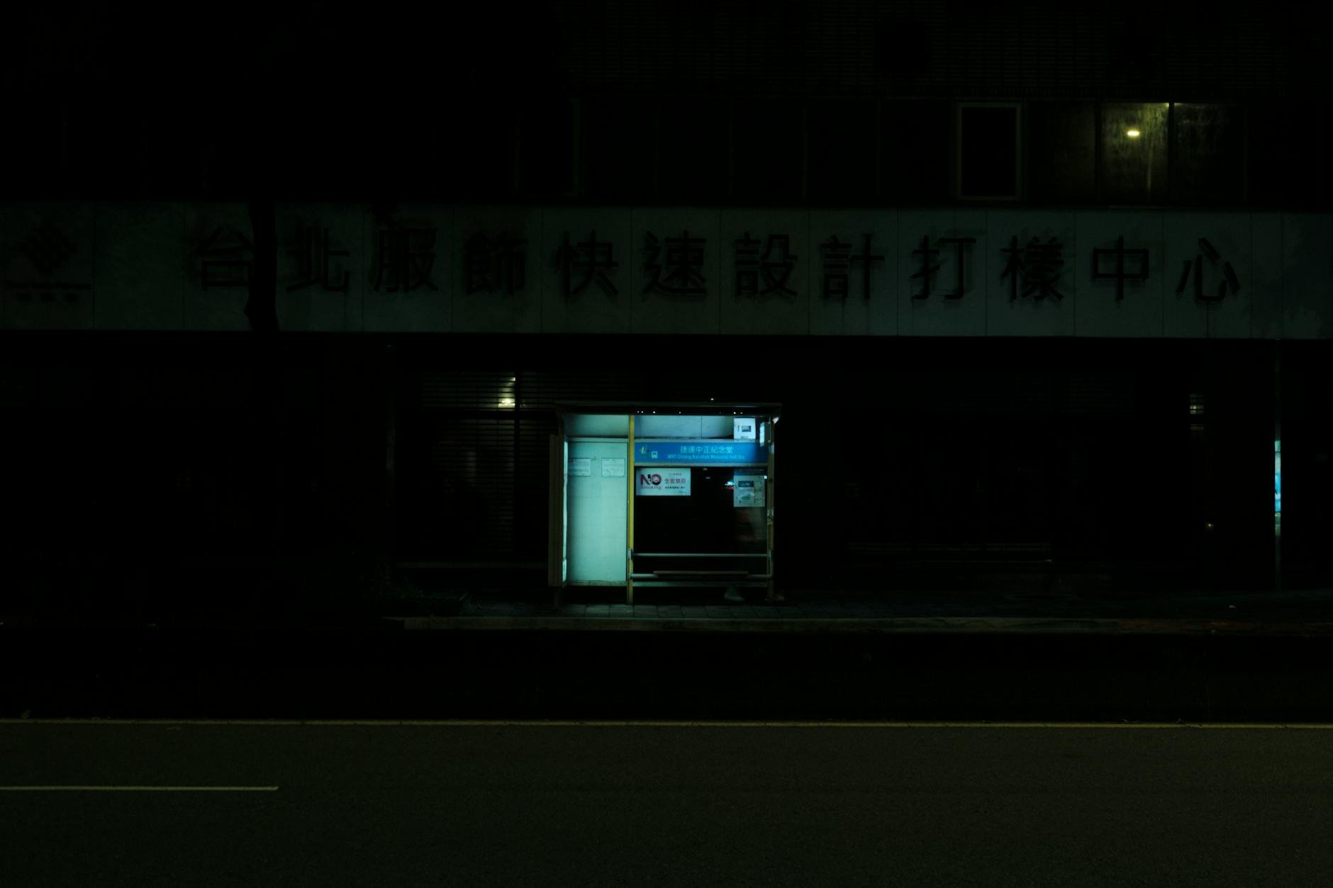 A dimly lit bus stop on a deserted street at night, emphasizing isolation and urban life.