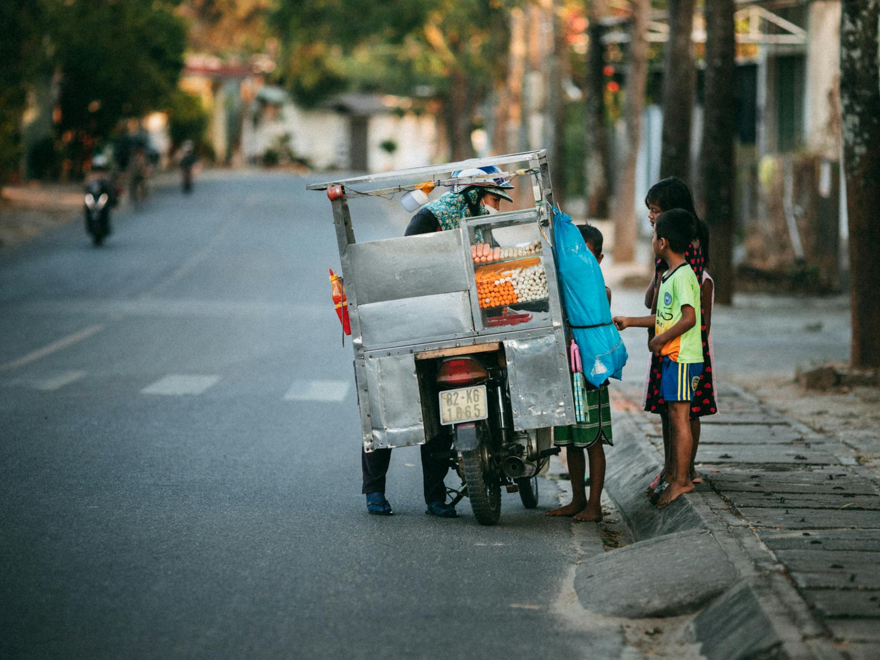 A roadside vendor on a scooter selling goods to local children in Kon Tum, Vietnam.