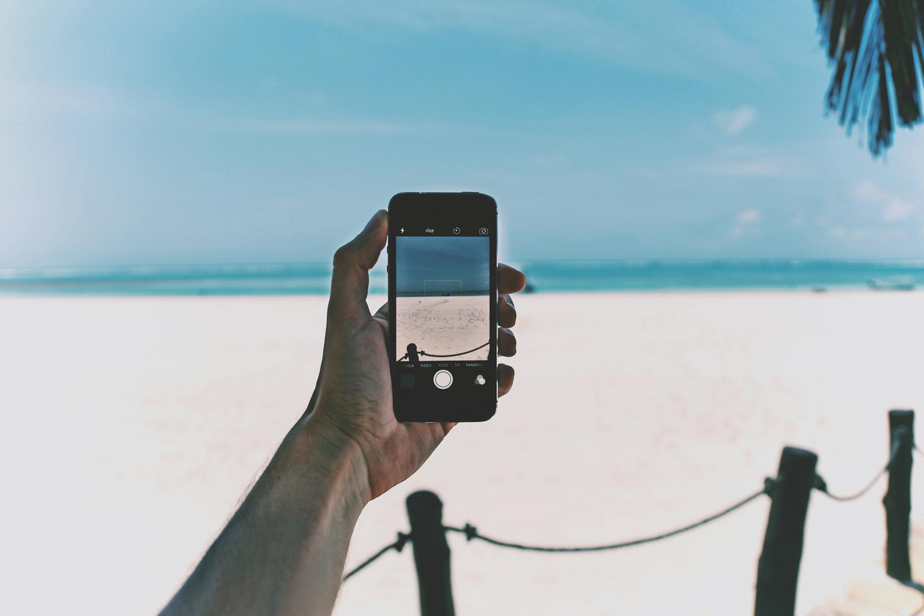 A hand holding a smartphone capturing a scenic beach view.
