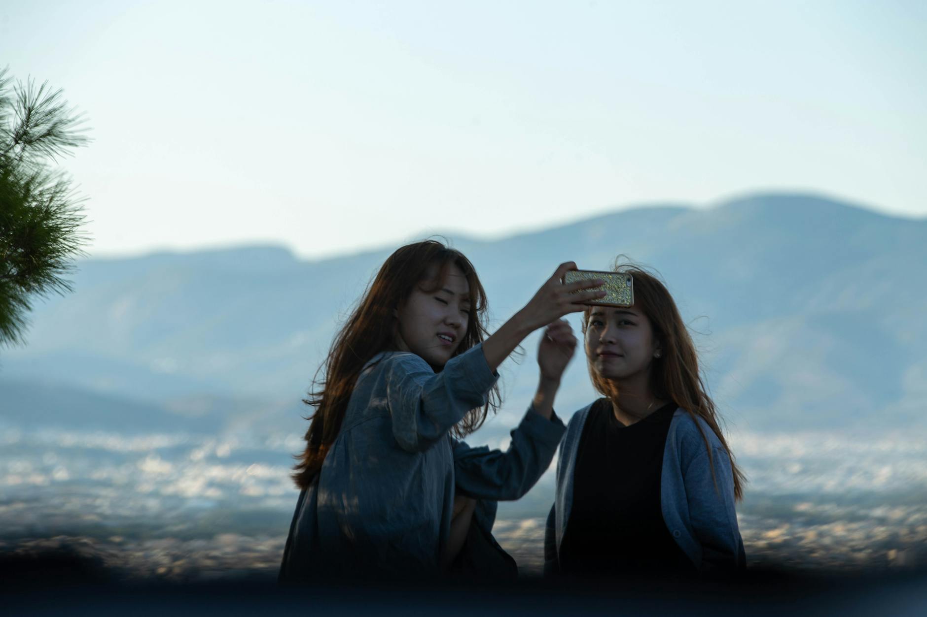 Two young women taking a selfie with scenic mountains in the background. Smiling and enjoying the day.