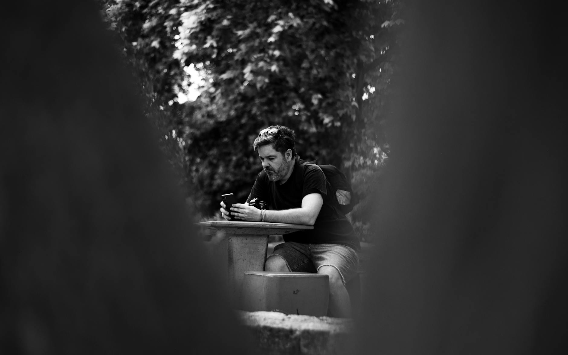 Candid black and white photo of a man sitting by himself in a Buenos Aires park, immersed in his phone.