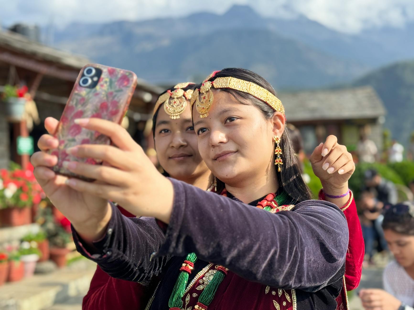 Two young adults in traditional attire taking a selfie against a mountain backdrop.