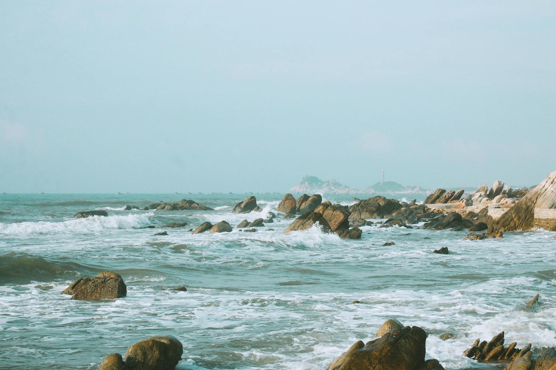 Tranquil view of rocky shoreline in Phan Thiết, Vietnam under a clear sky.