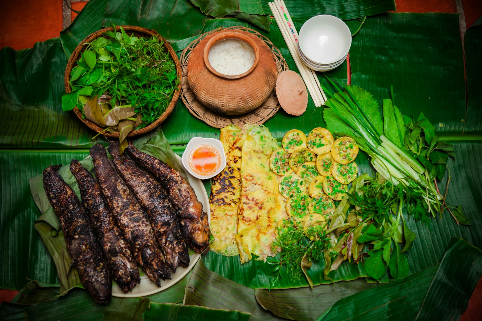 Delicious traditional Vietnamese meal featuring grilled fish, rice cakes, and fresh herbs on banana leaves.