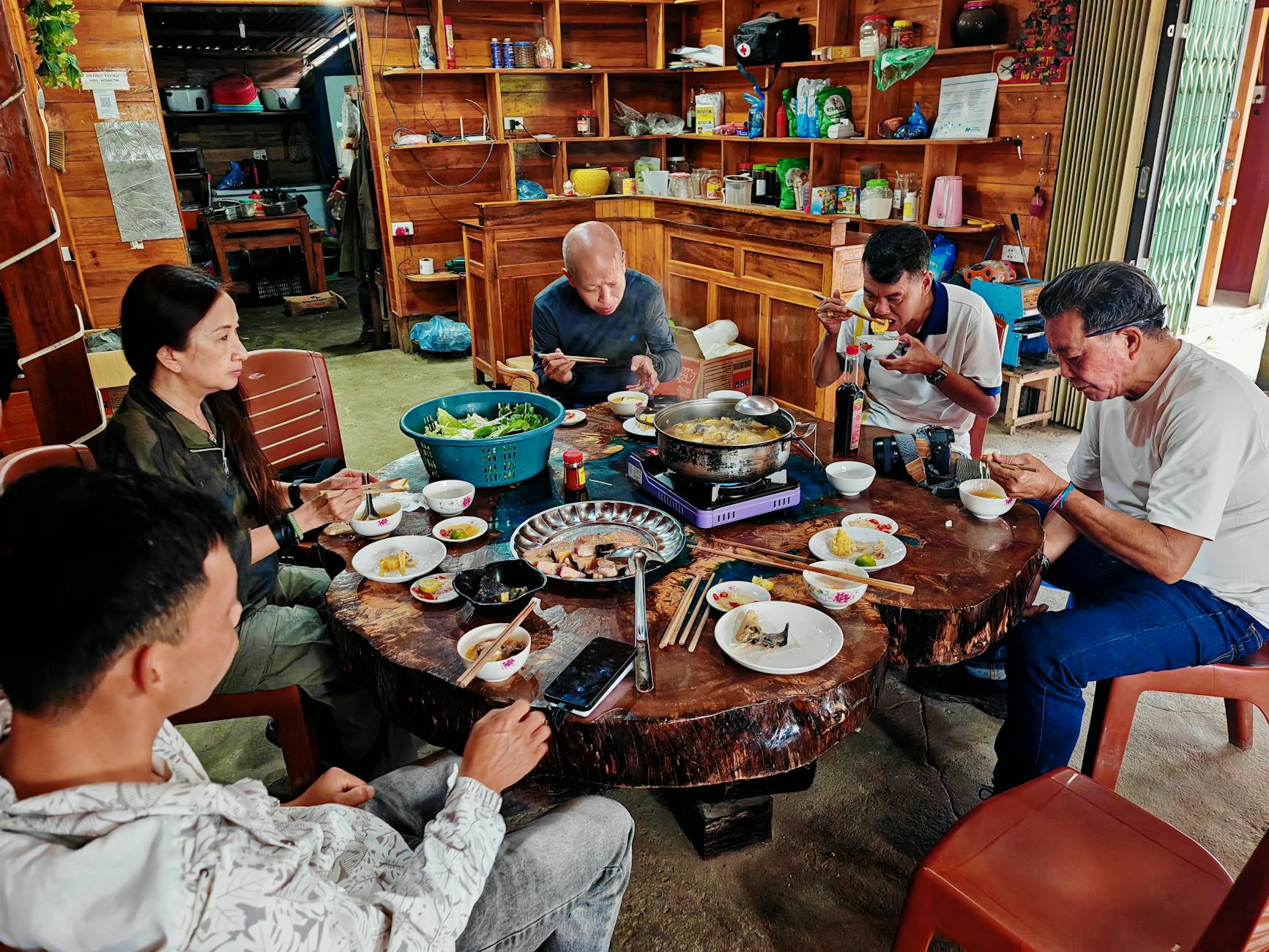 A group of adults enjoying a traditional hot pot meal in a warm, rustic kitchen setting.