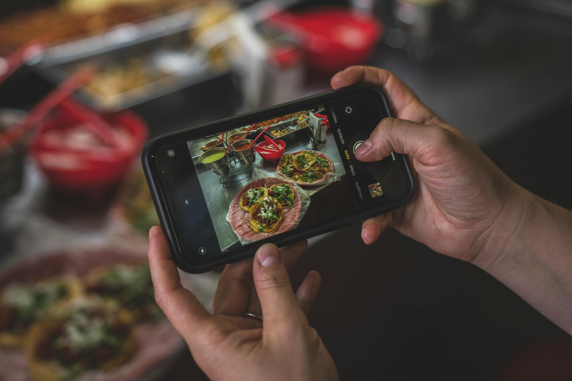 Hands holding a smartphone capturing tacos, showcasing vibrant Mexican street food.