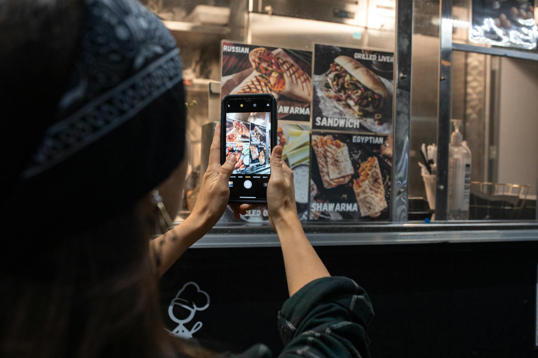 Photograph of a person taking a picture of a street food menu at night.