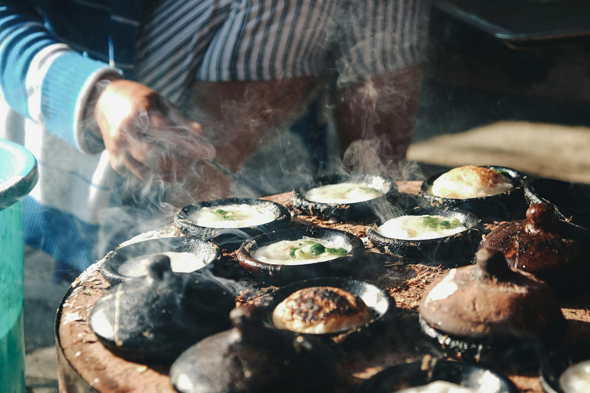 Delicious Vietnamese banh can being cooked outdoors in clay pots, showcasing authentic culinary techniques.