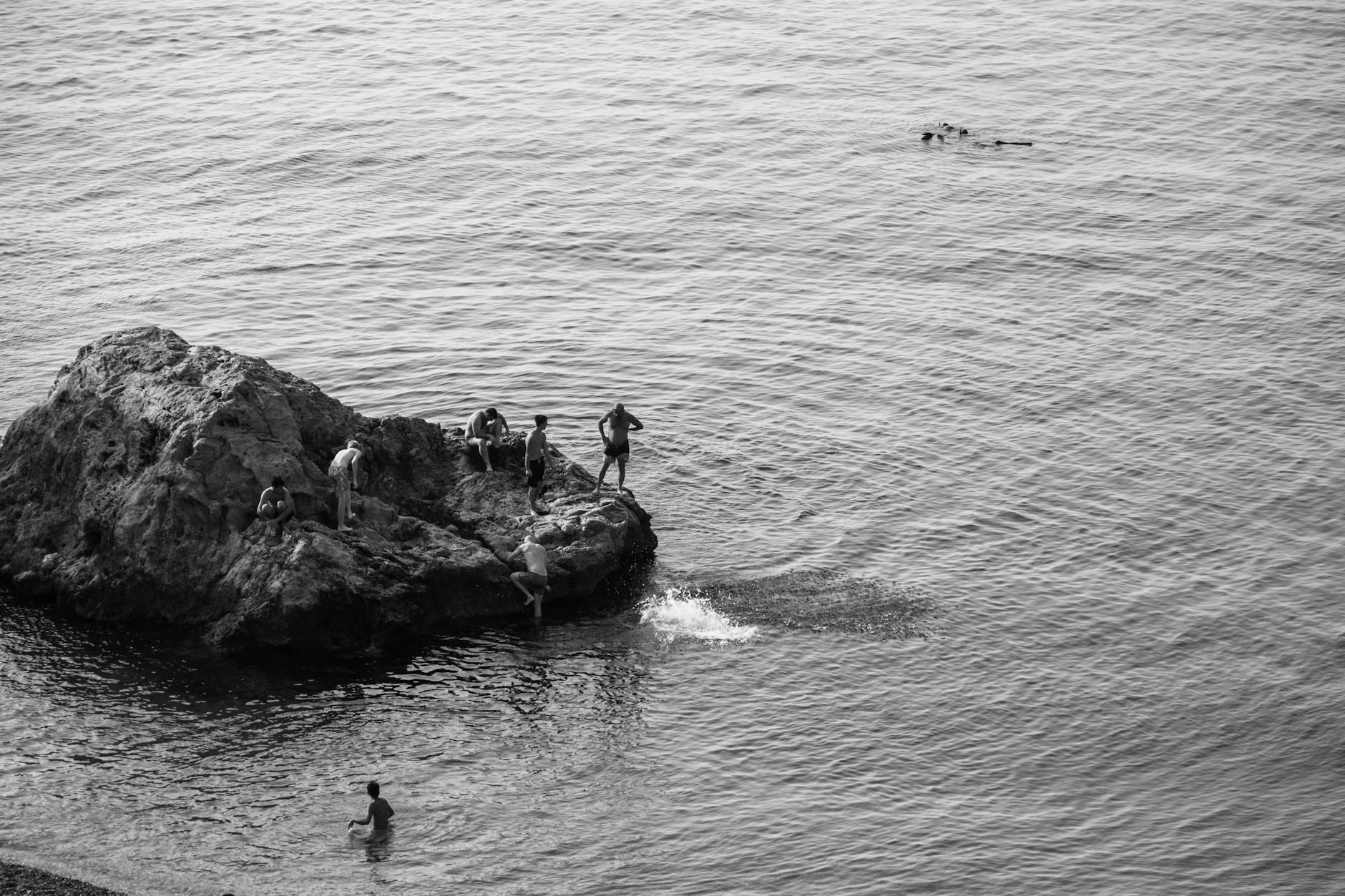 A group of individuals relaxing on a rocky sea shore in monochrome.
