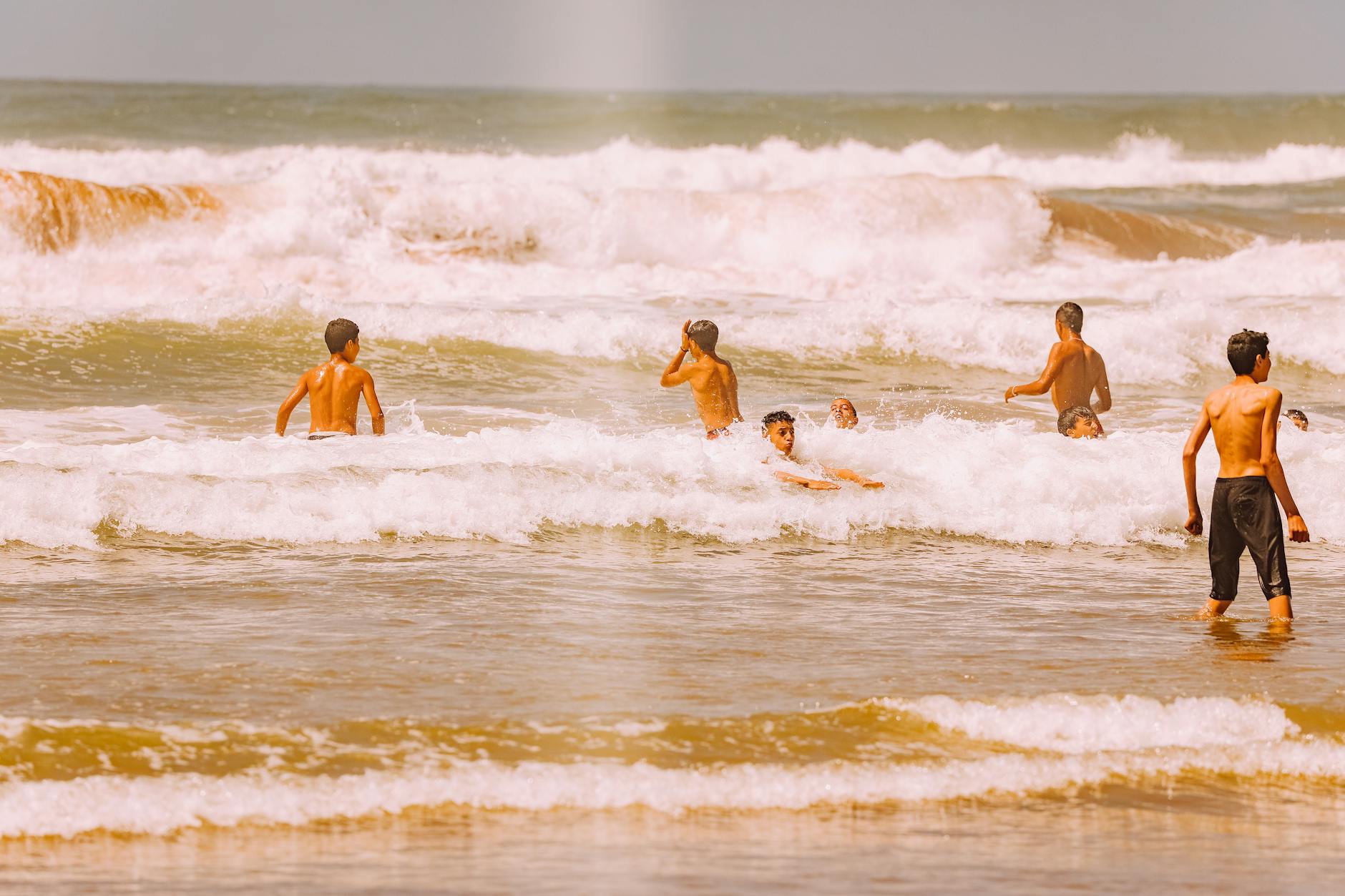 A group of people having fun in the ocean waves at a sandy beach during daytime, capturing the essence of summer leisure.