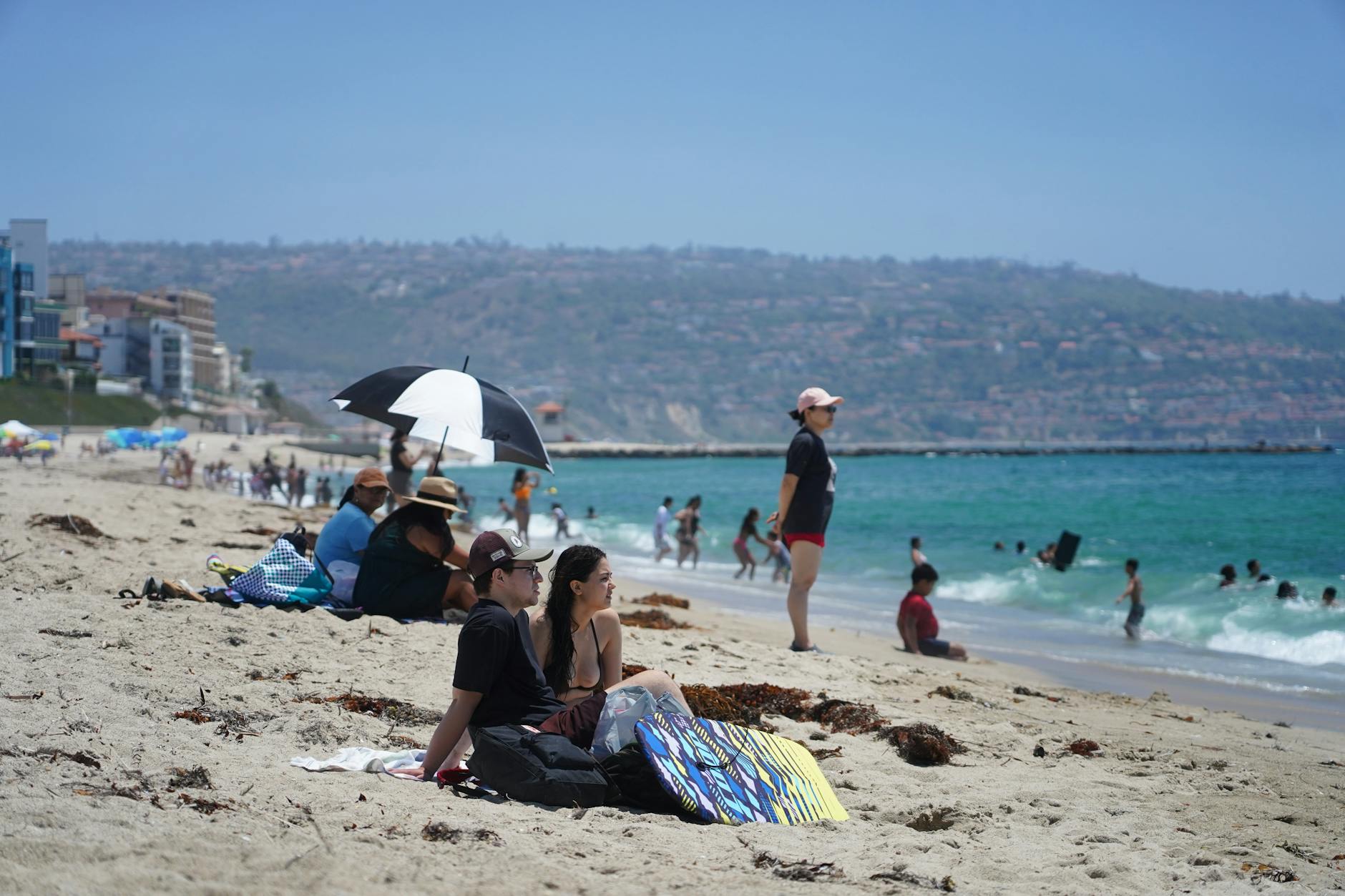 People enjoying a sunny day at a beachfront resort, relaxing on the sand and swimming.