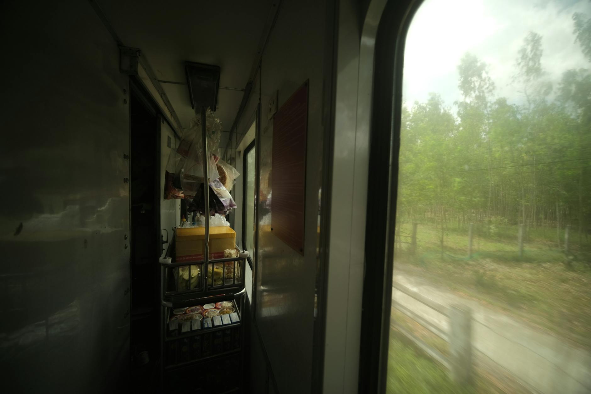 A food cart inside a train with a view of green countryside passing by.