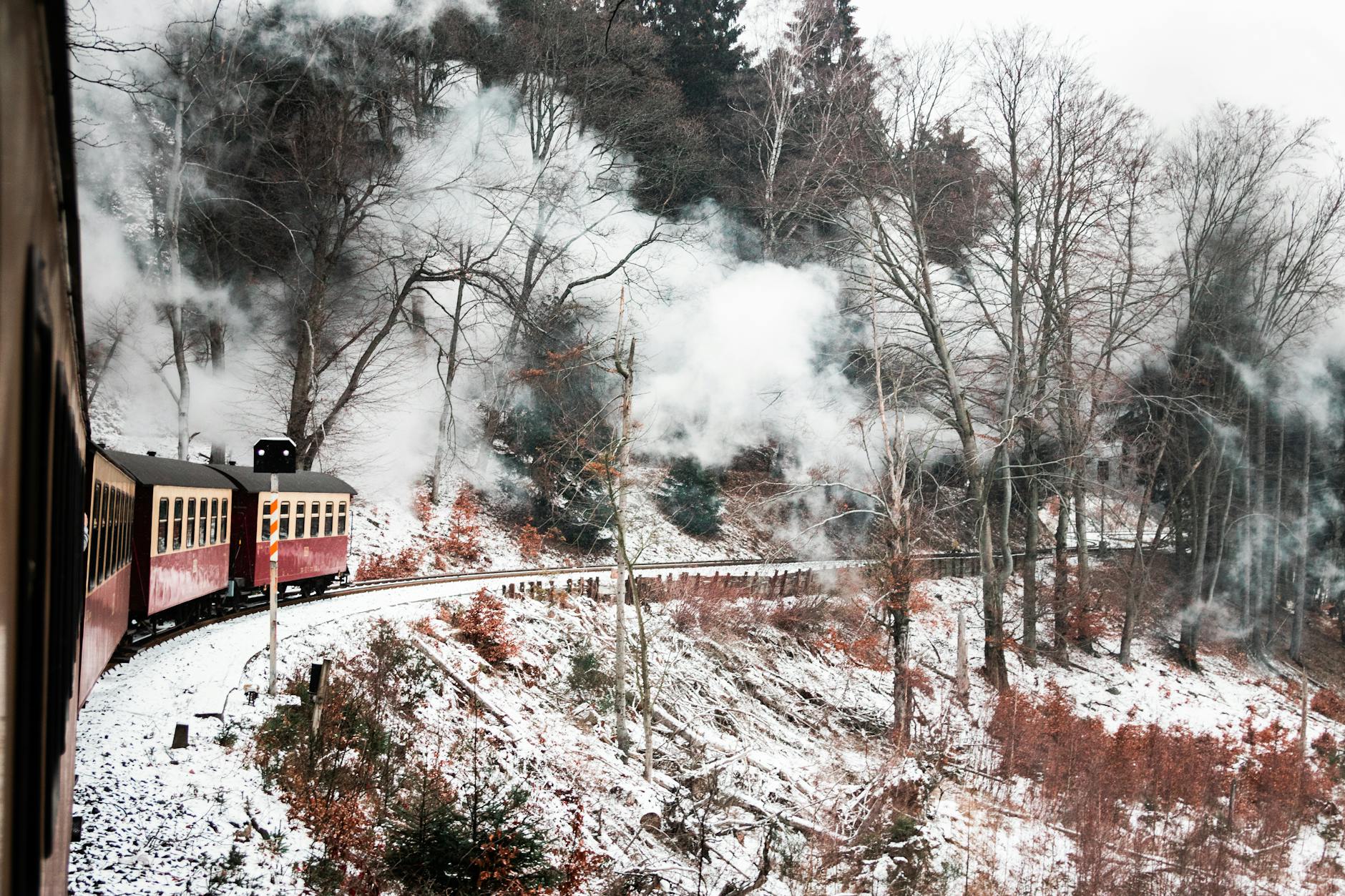 A nostalgic steam train travels through a snowy forest landscape, showcasing seasonal beauty and winter charm.