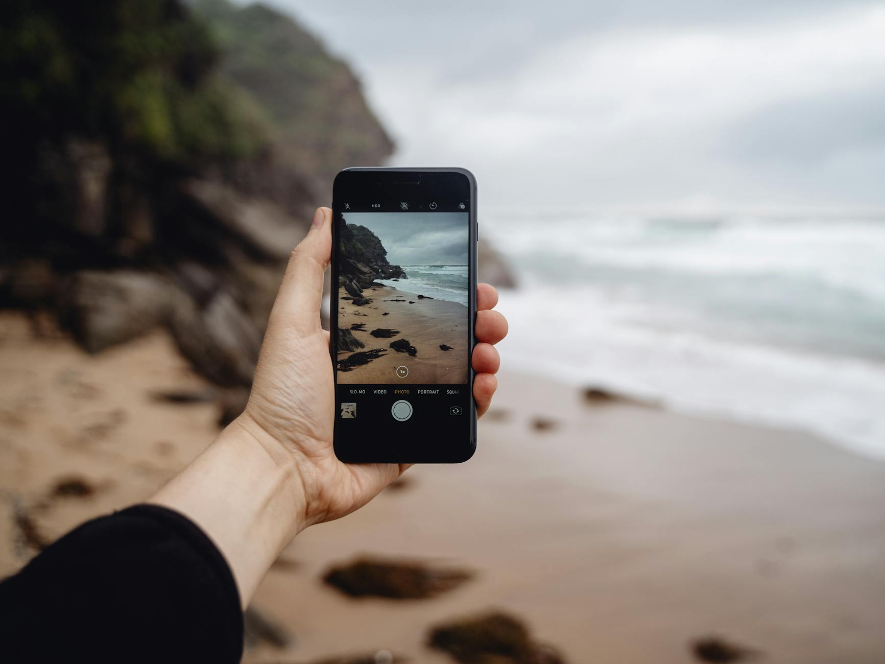 Hand holding smartphone capturing Stanwell Park's rocky beach. Outdoor photography at its best.