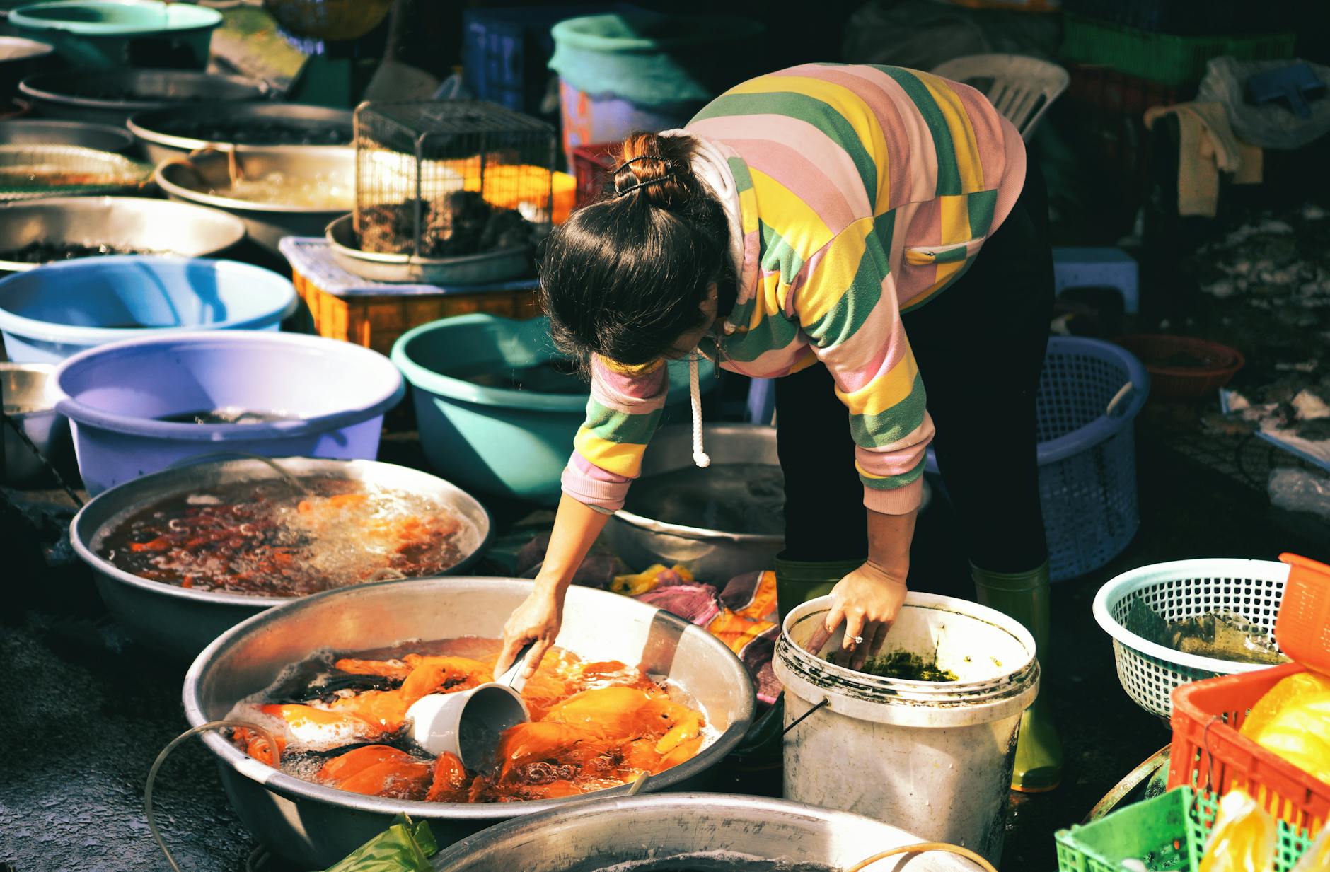 Woman at a bustling Vietnamese fish market tending to fresh seafood in colorful basins.