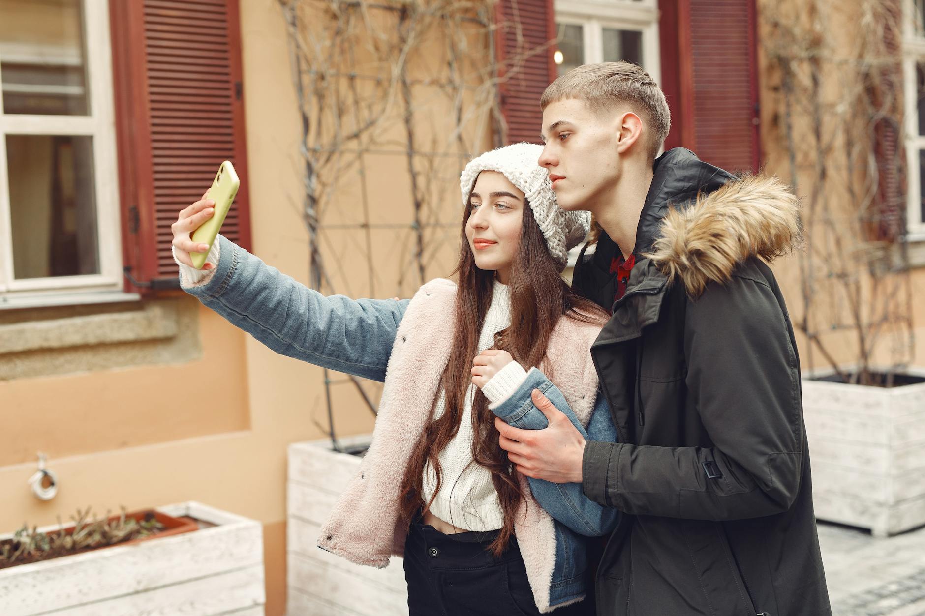 A young couple takes a selfie outdoors, enjoying a winter day together in a cozy setting.