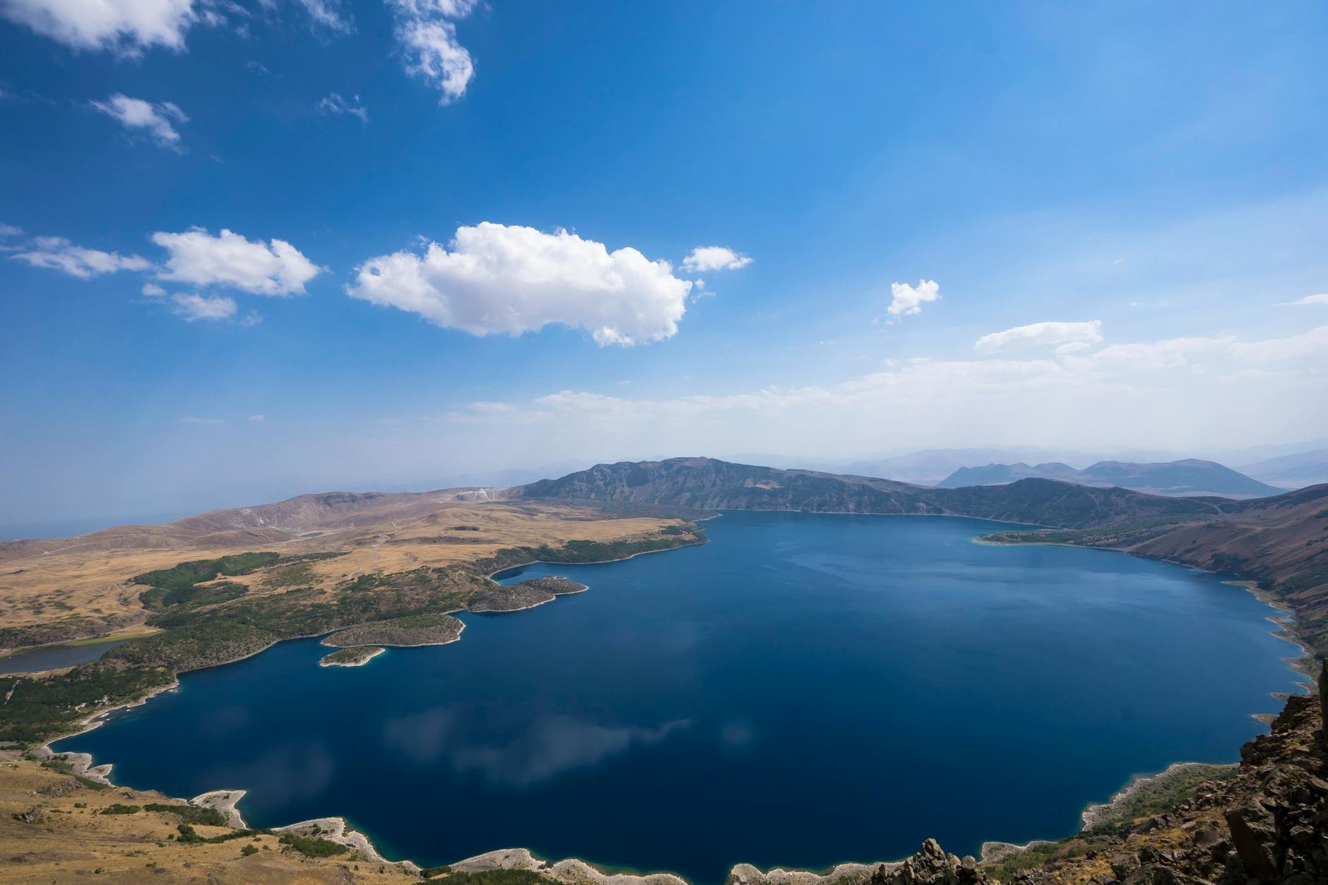 Discover the beauty of a serene crater lake surrounded by vast landscapes under a clear blue sky.