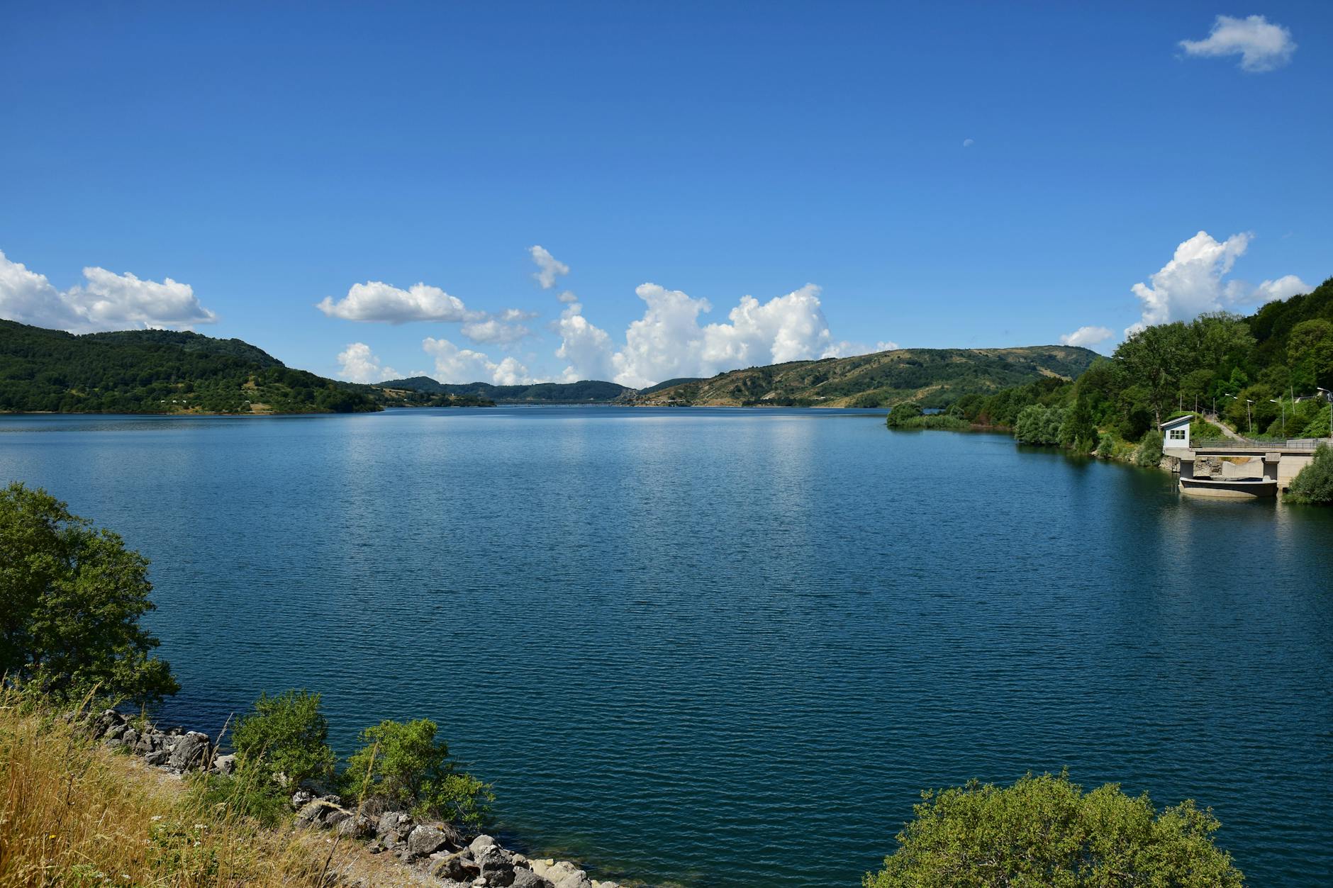 Peaceful aerial view of Lake Campotosto, surrounded by hills and lush greenery under a clear blue sky.