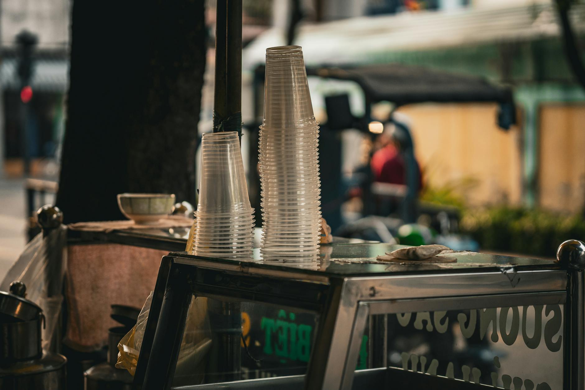 Street vendor cart in Ho Chi Minh City with stacks of plastic cups and bustling street in the background.